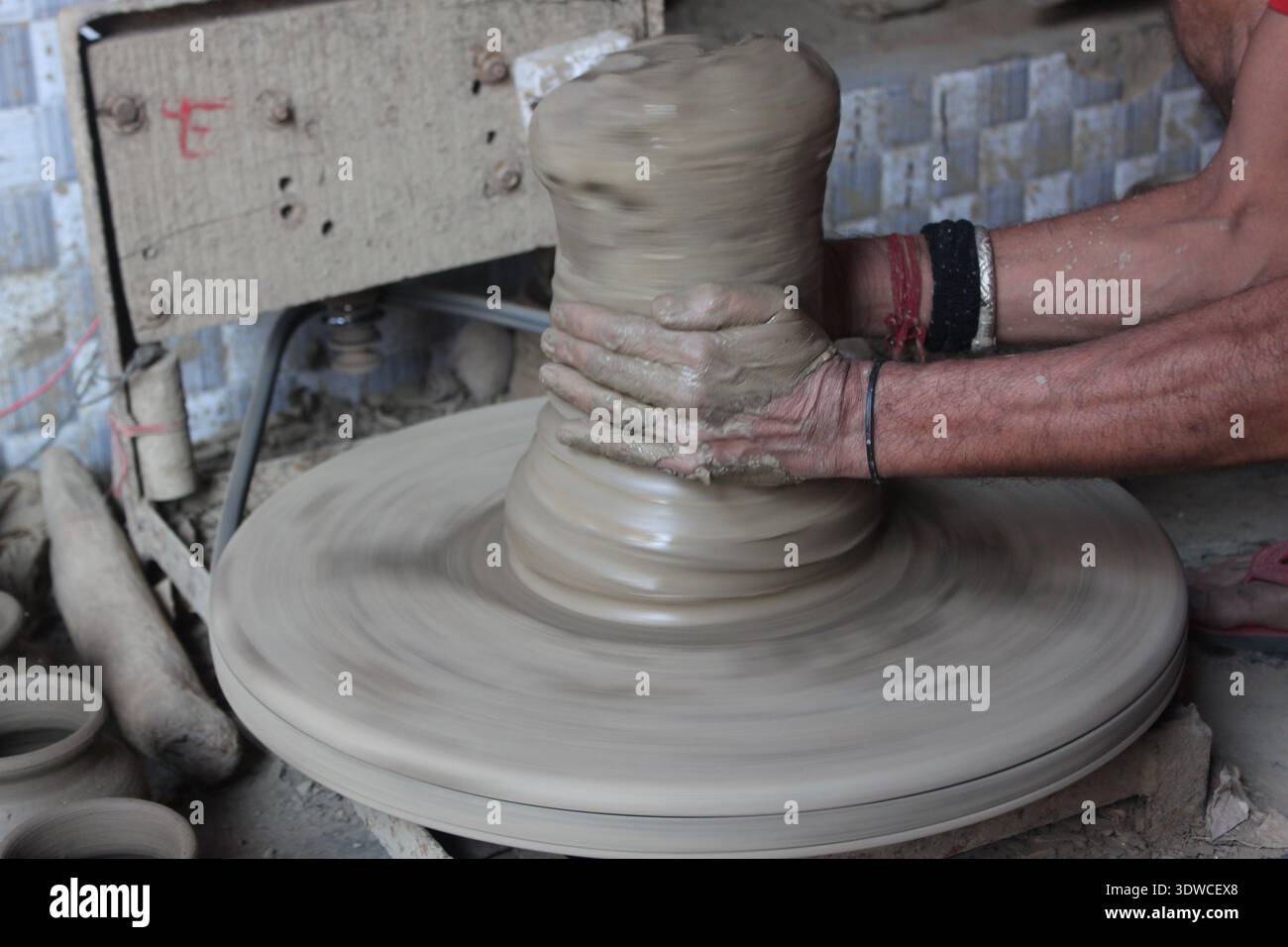 Indian artisan forms a clay pot on a fast‑spinning potters' wheel in Delhi, India, showing traditional pottery making (New Delhi 2019). Stock Photo