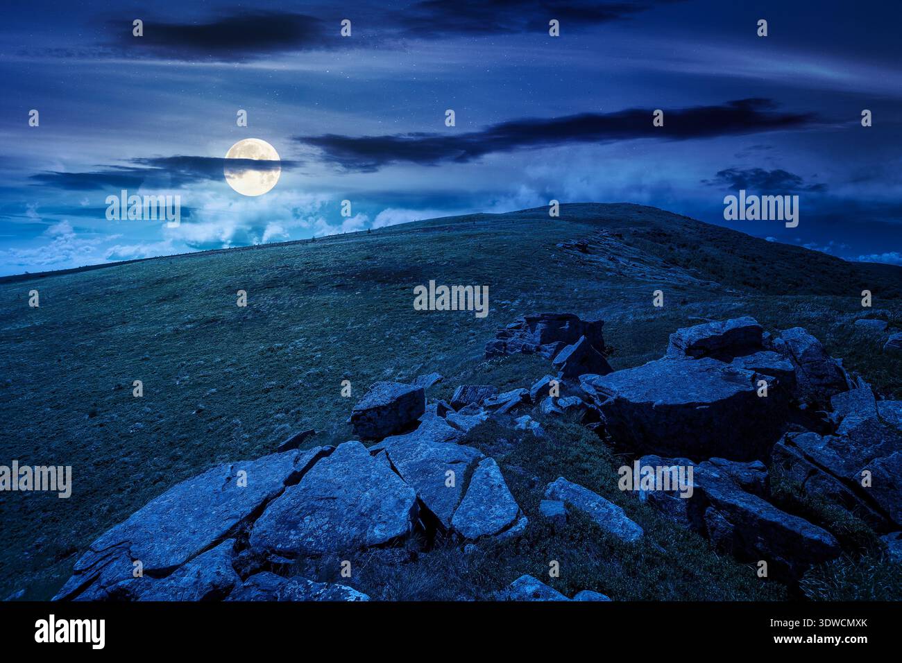 rocks and rolling hills in mountain landscape in summer at night. full moon over scenery with green grass on alpine meadow under dark sky with clouds. Stock Photo