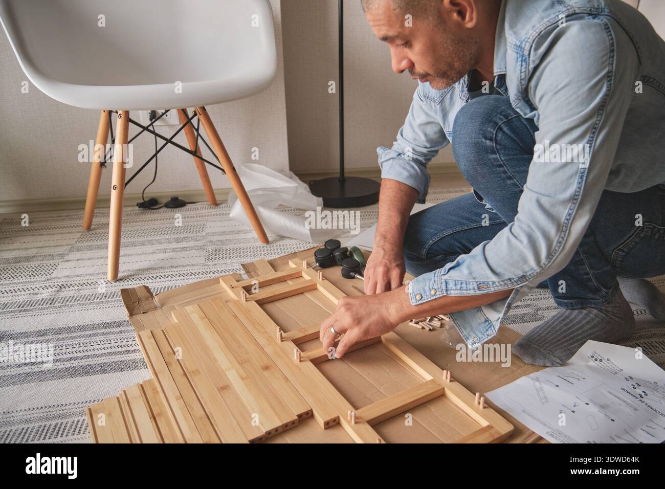 Man kneeling, assembling flat pack furniture using instructions on the floor Stock Photo