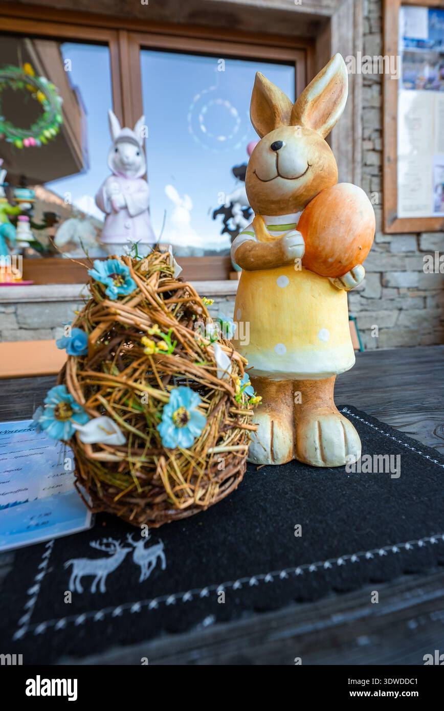 Ceramic bunny with orange Easter egg on rustic table in cafe setting Stock Photo
