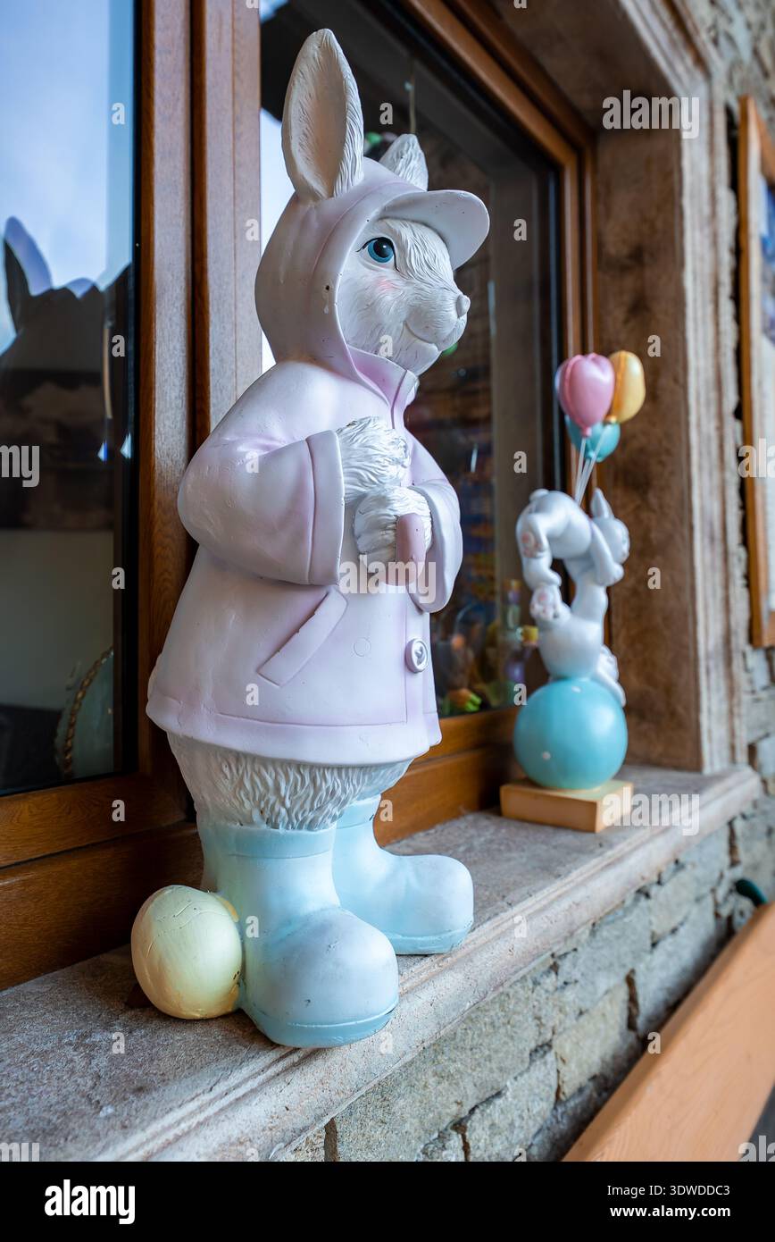 Easter bunny statue in raincoat on stone windowsill with egg Stock Photo