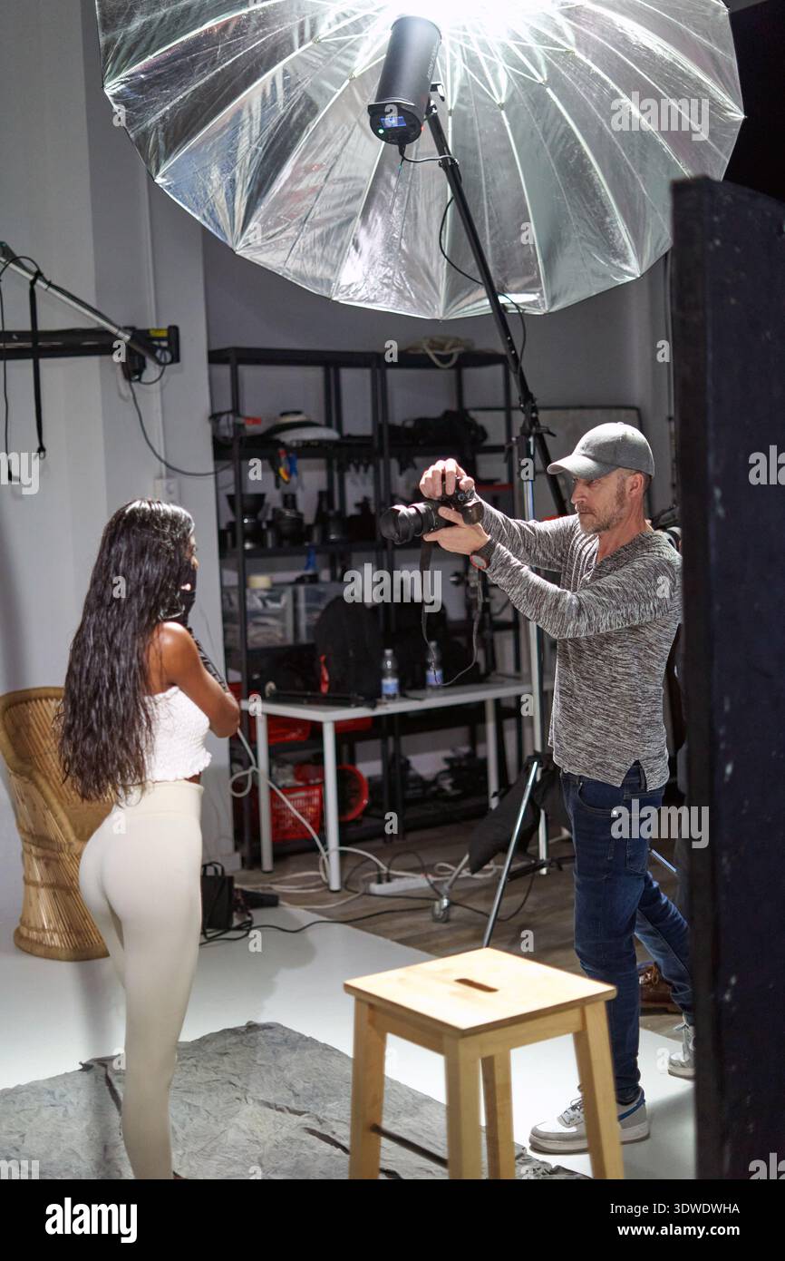 A model poses for a photoshoot in a studio while a photographer ...