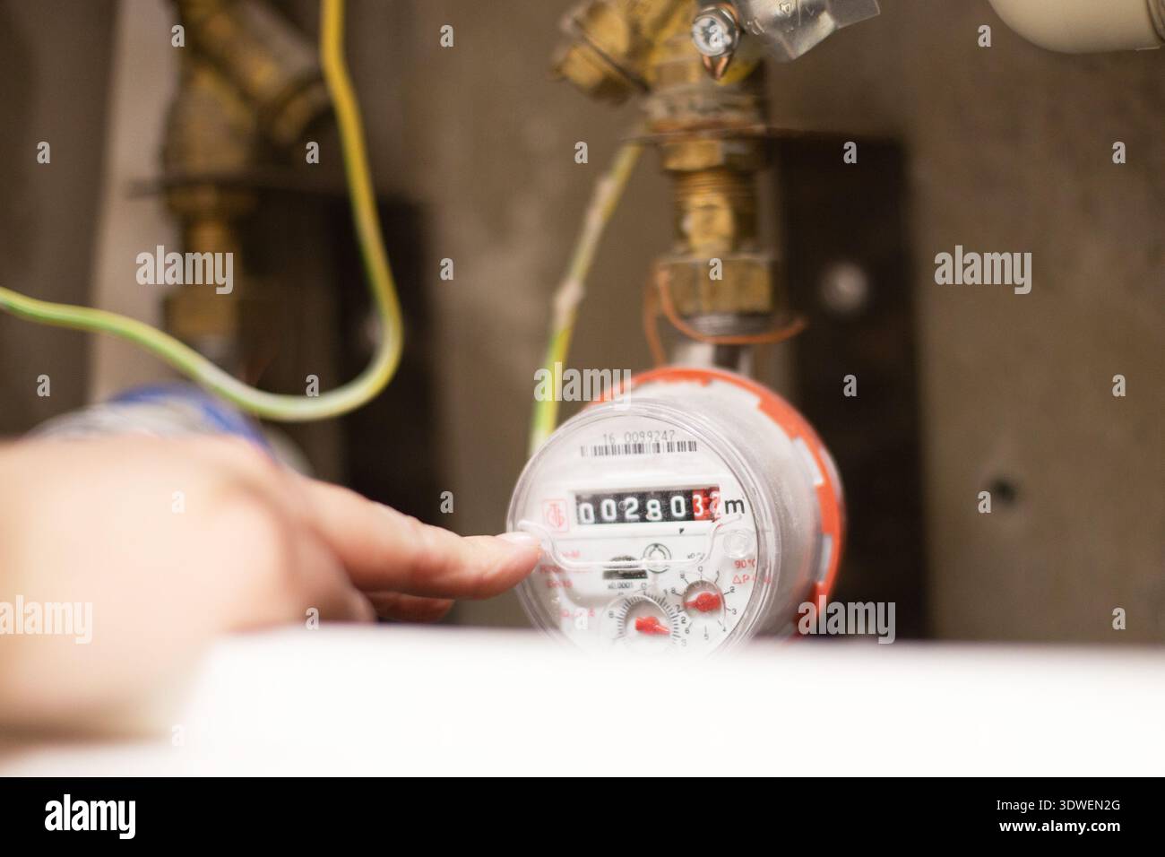 Hand checking the water meter display with current reading and pipes in ...