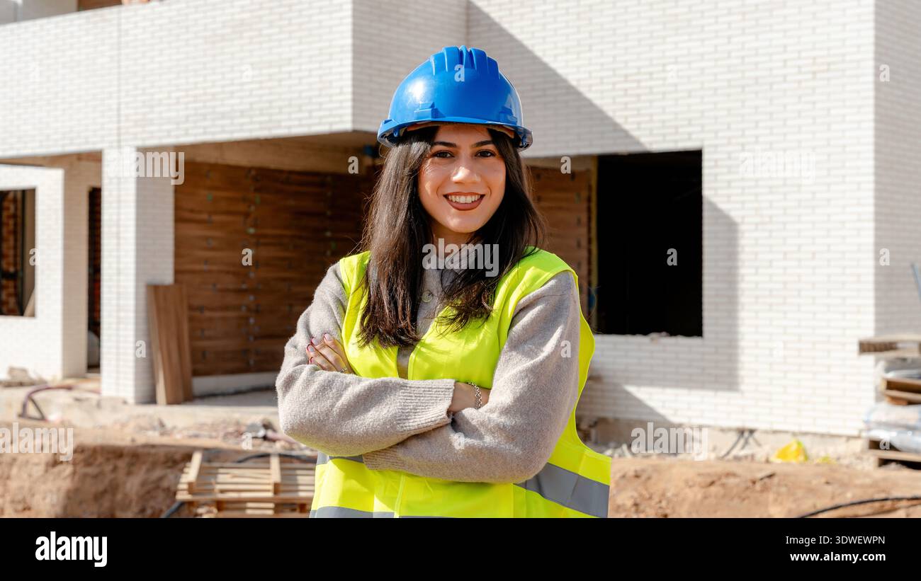 A technical engineer stands confidently on a construction site, wearing a hardhat and safety vest, overseeing the building process and ensuring projec Stock Photo