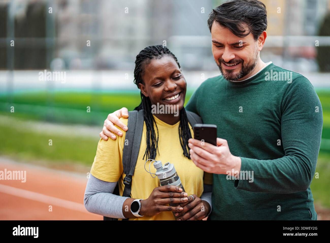 Diverse couple smiling using smartphone on running track Stock Photo