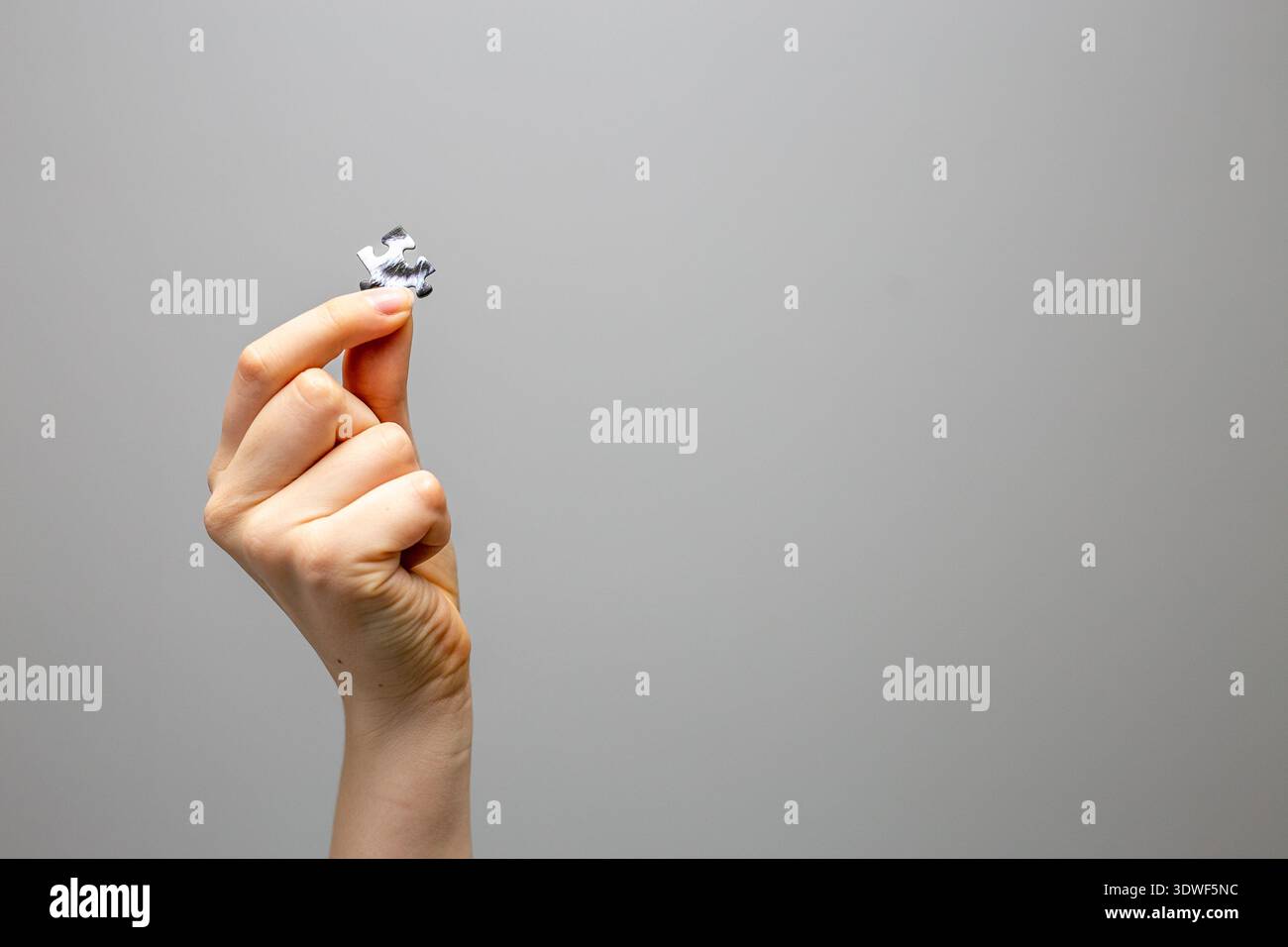 Hand holding a single jigsaw puzzle piece against a plain background. Concept image symbolizing problem solving, final solution, completing a project Stock Photo