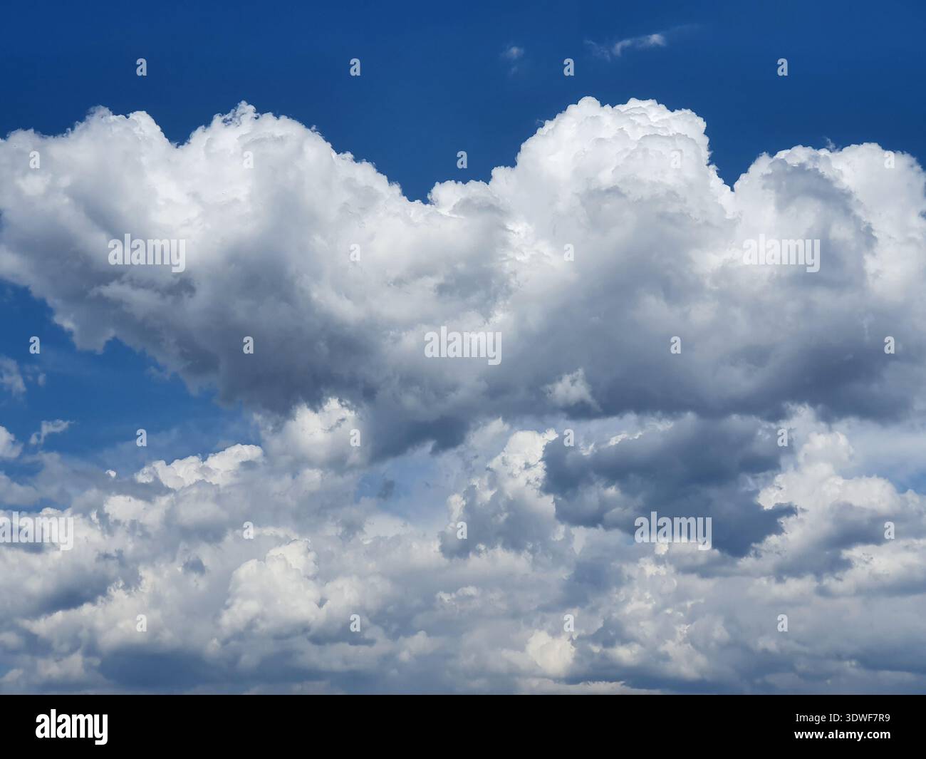 Massive white cumulus clouds form a dramatic textured sky against a deep-blue backdrop, suggesting summer weather, openness and atmosphere, suitable f Stock Photo