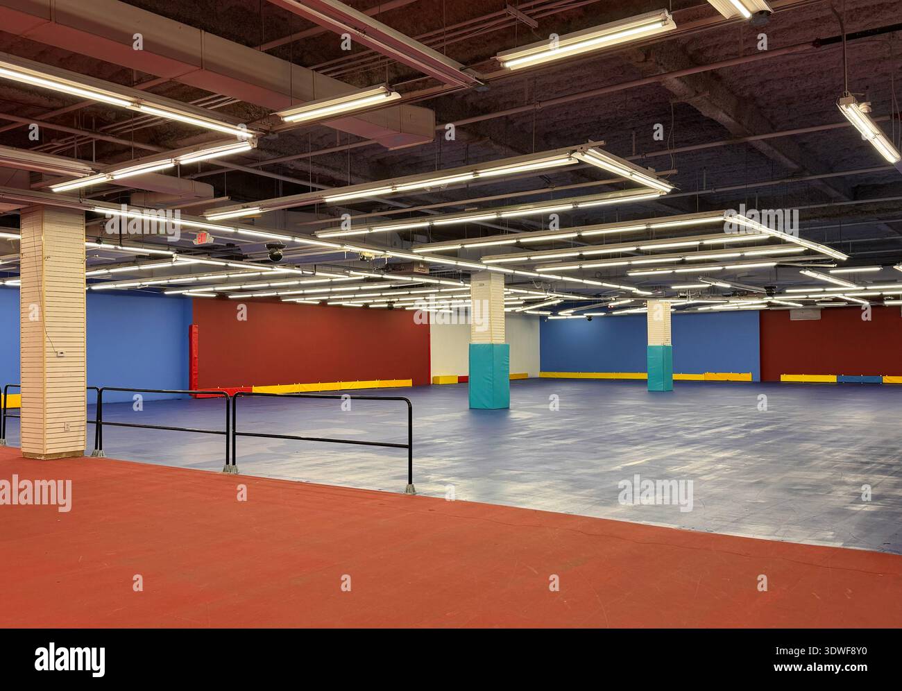 Empty indoor roller rink with colorful walls and fluorescent ceiling lights, wide open skating floor and railings. - Smartphone Captured Stock Image