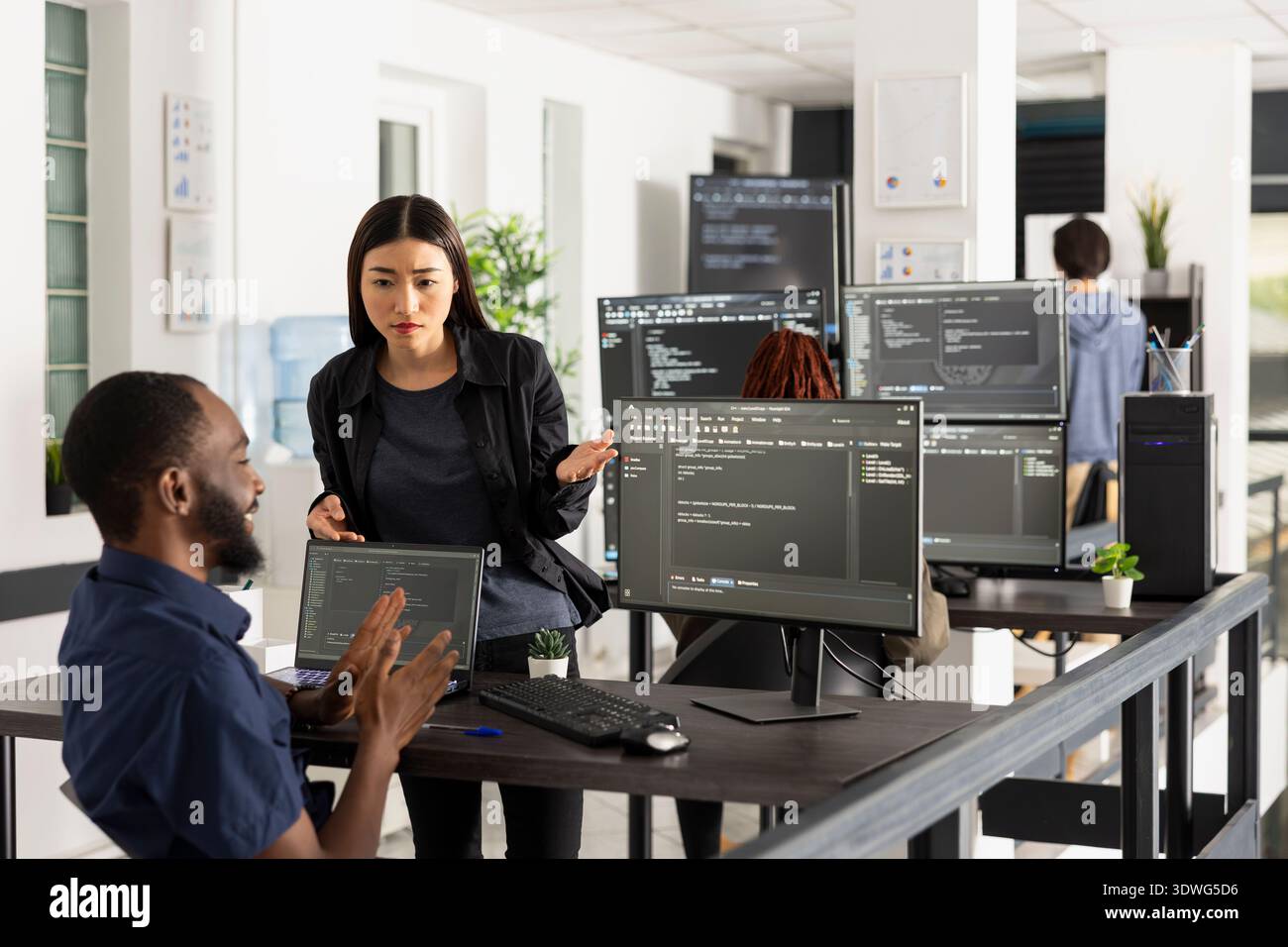 Adult programmers review website functionality together, comparing code on computer screen in startup office. Focused discussion reflects teamwork, innovation and software development culture. Stock Photo