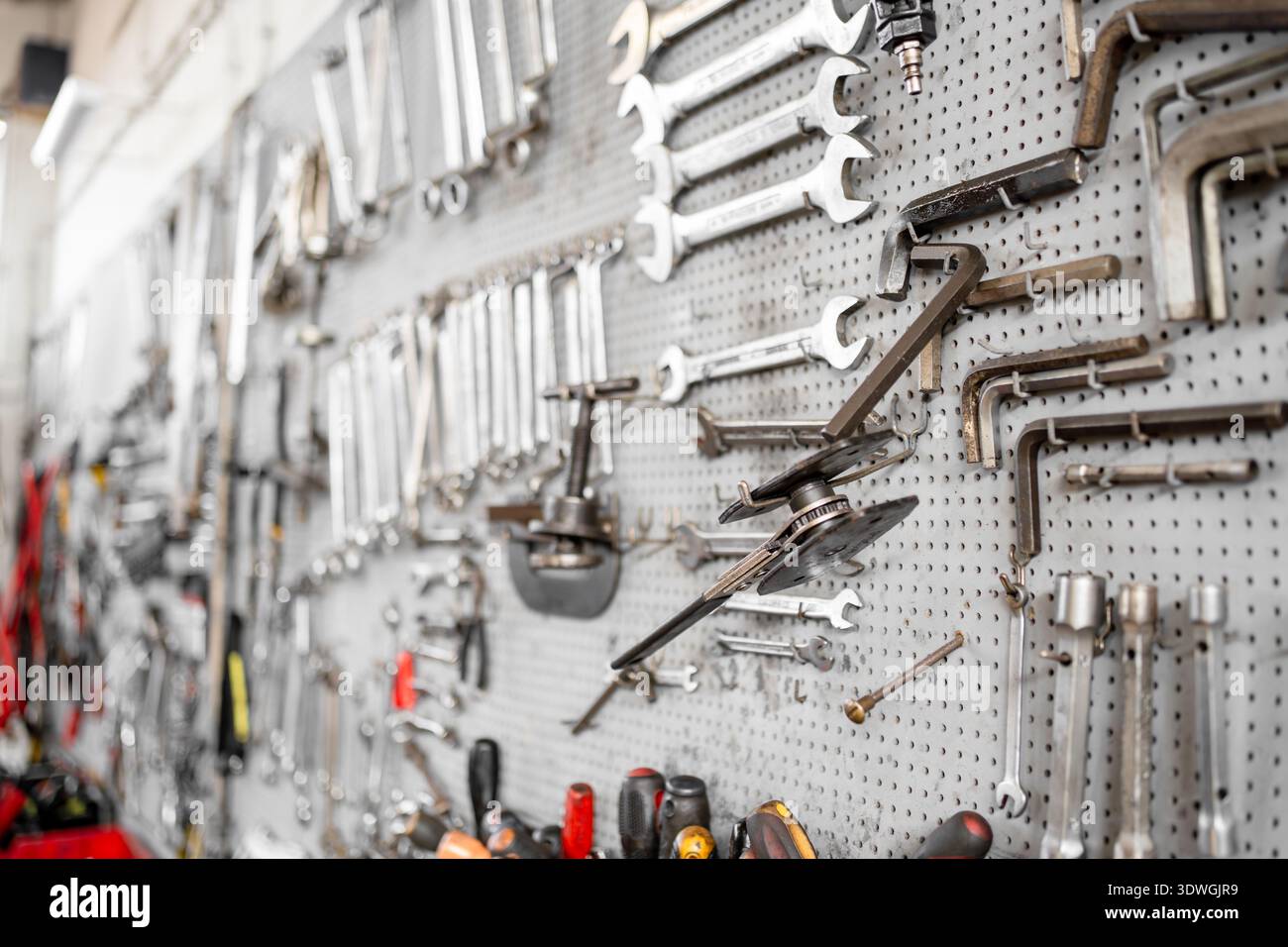 Various hand tools neatly arranged on perforated wall inside workshop. Organized work environment and industrial maintenance concept Stock Photo
