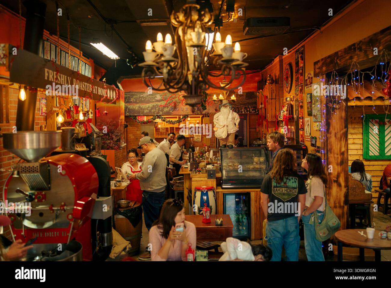 Customers waiting at La Colada Gourmet coffee shop interior featuring a unique porcelain cup chandelier and a red roasting machine. Stock Photo