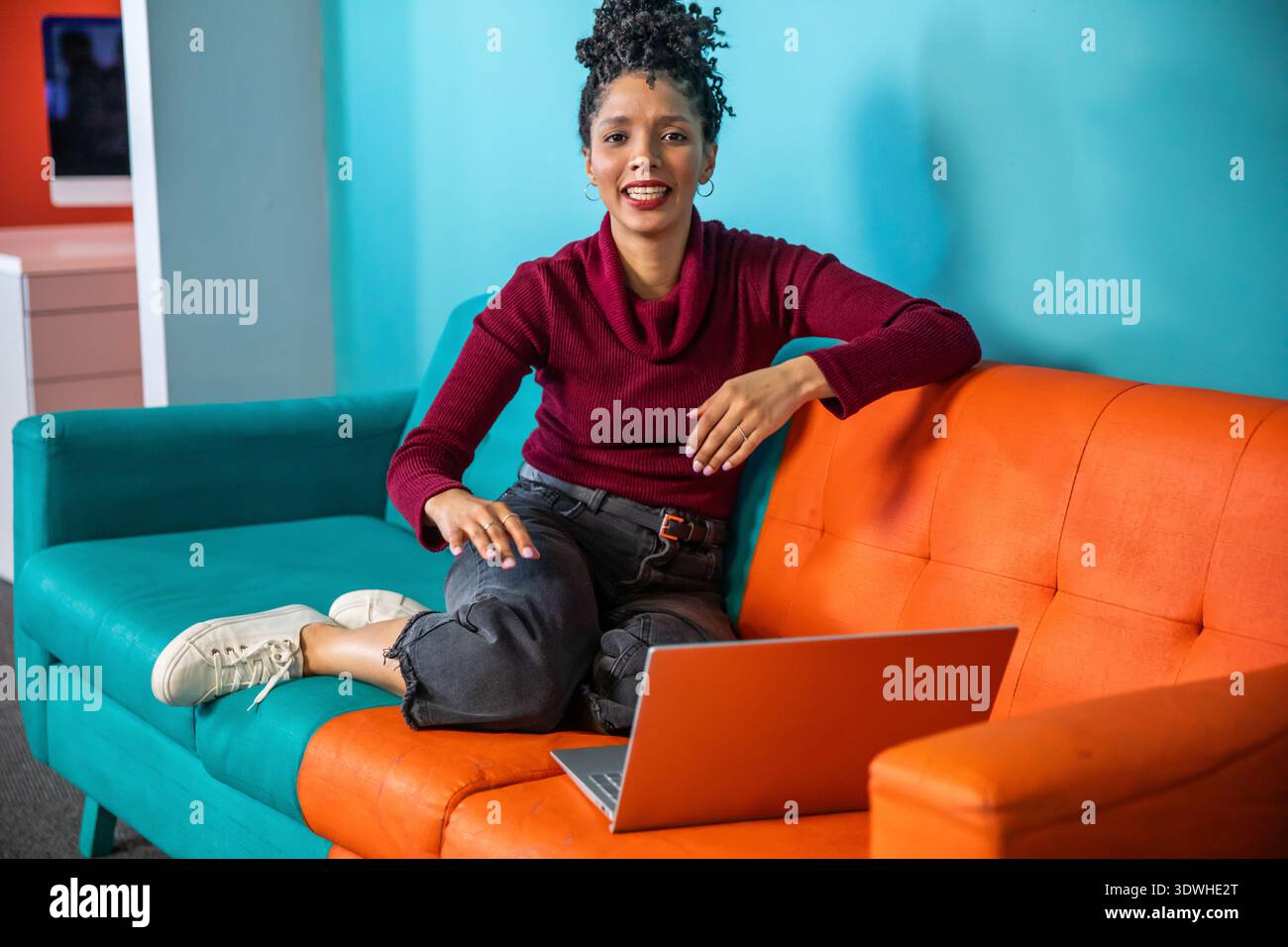 African American woman sitting on two-tone sectional sofa at home using silver laptop Stock Photo
