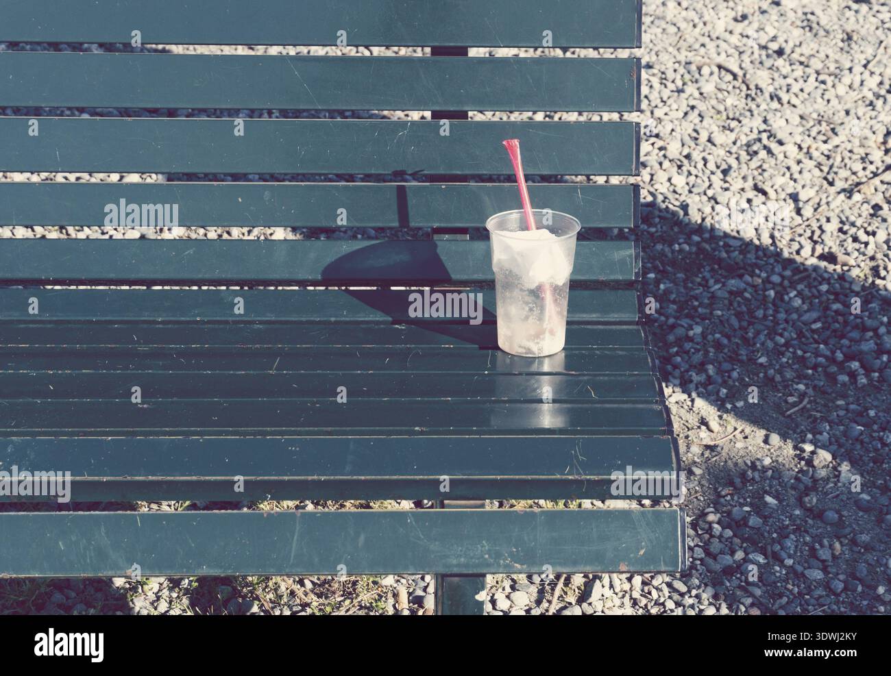 Disposable plastic drinks cup with straw lying on bench Stock Photo