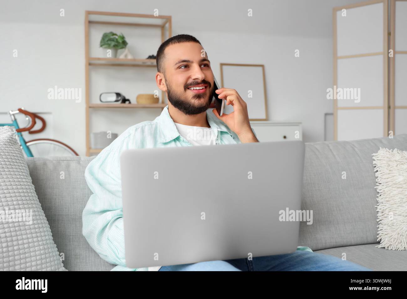 Young man working with laptop while talking on mobile phone Stock Photo
