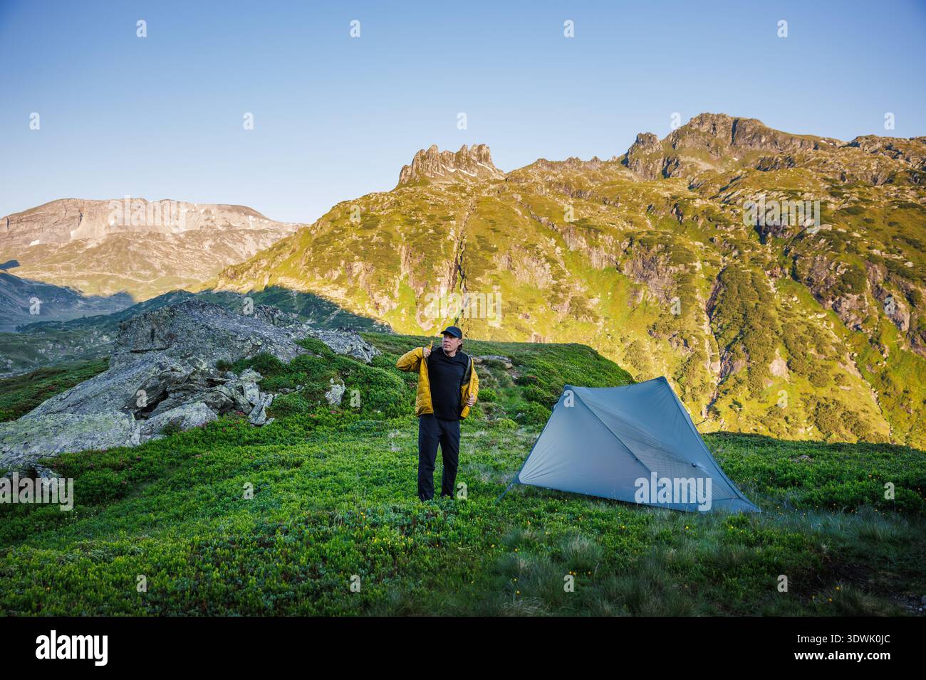 Wilderness Setting Wild camping under mountain peaks. Solo hiker standing at ultralight ...
