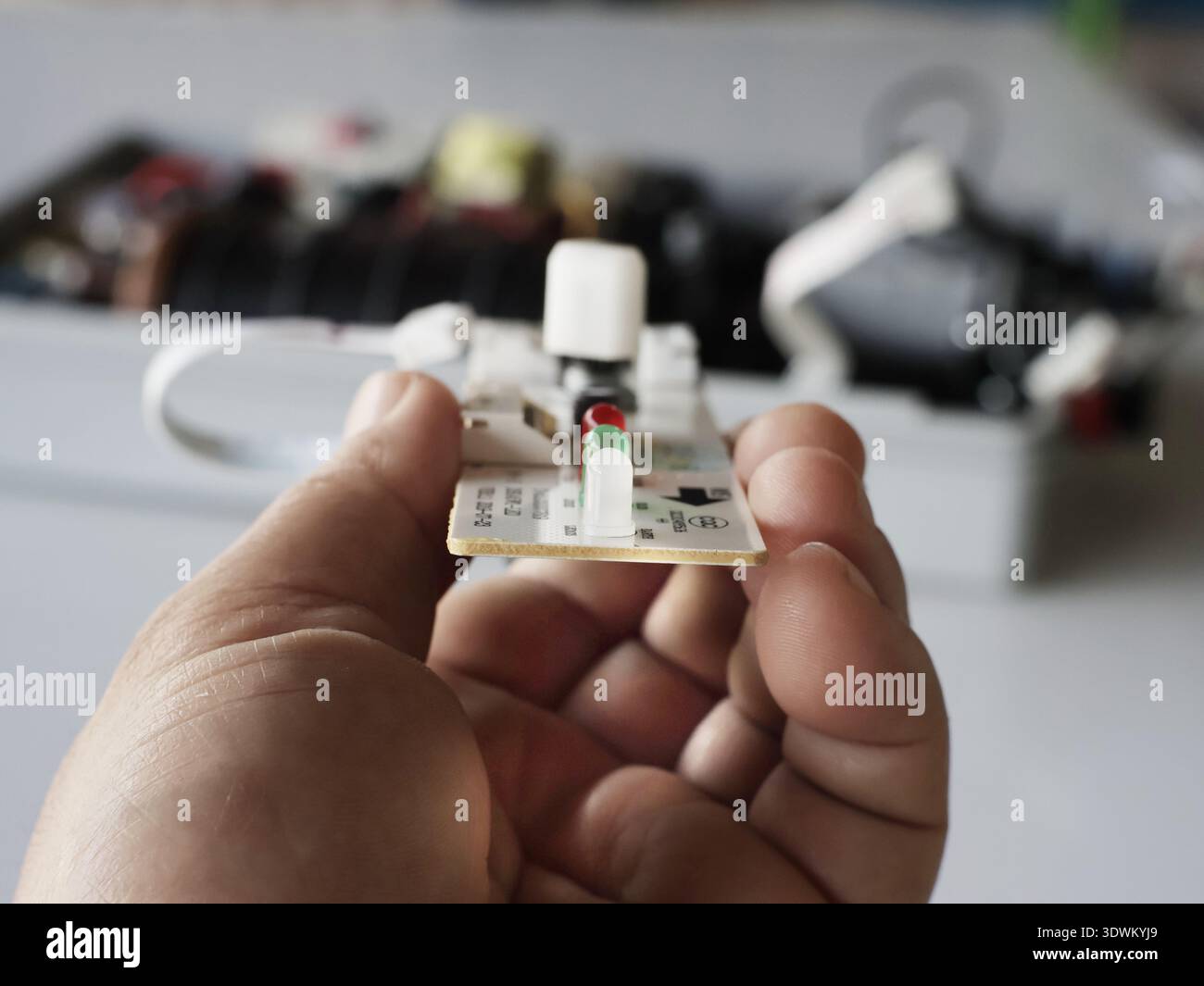 The image shows a small printed circuit board (PCB) held in a hand, containing electronic components. Stock Photo