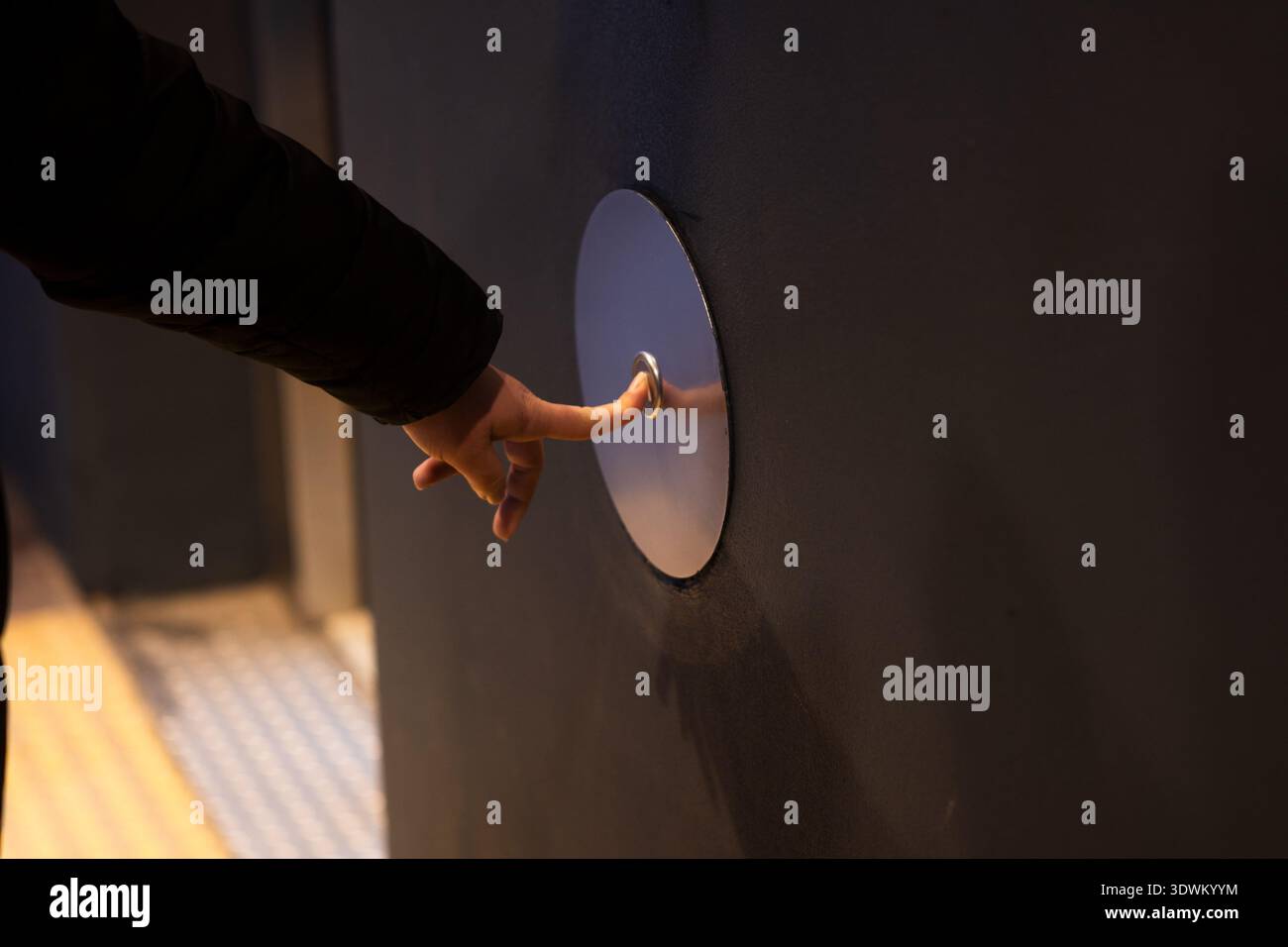 Human hand pressing a sleek, round, metallic button for an elevator or automatic door Stock Photo