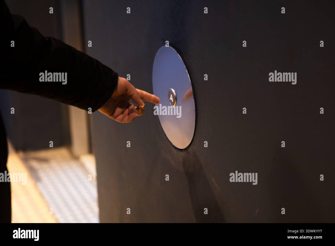 Person's hand reaching and pressing a circular floor selection button inside an elevator Stock Photo