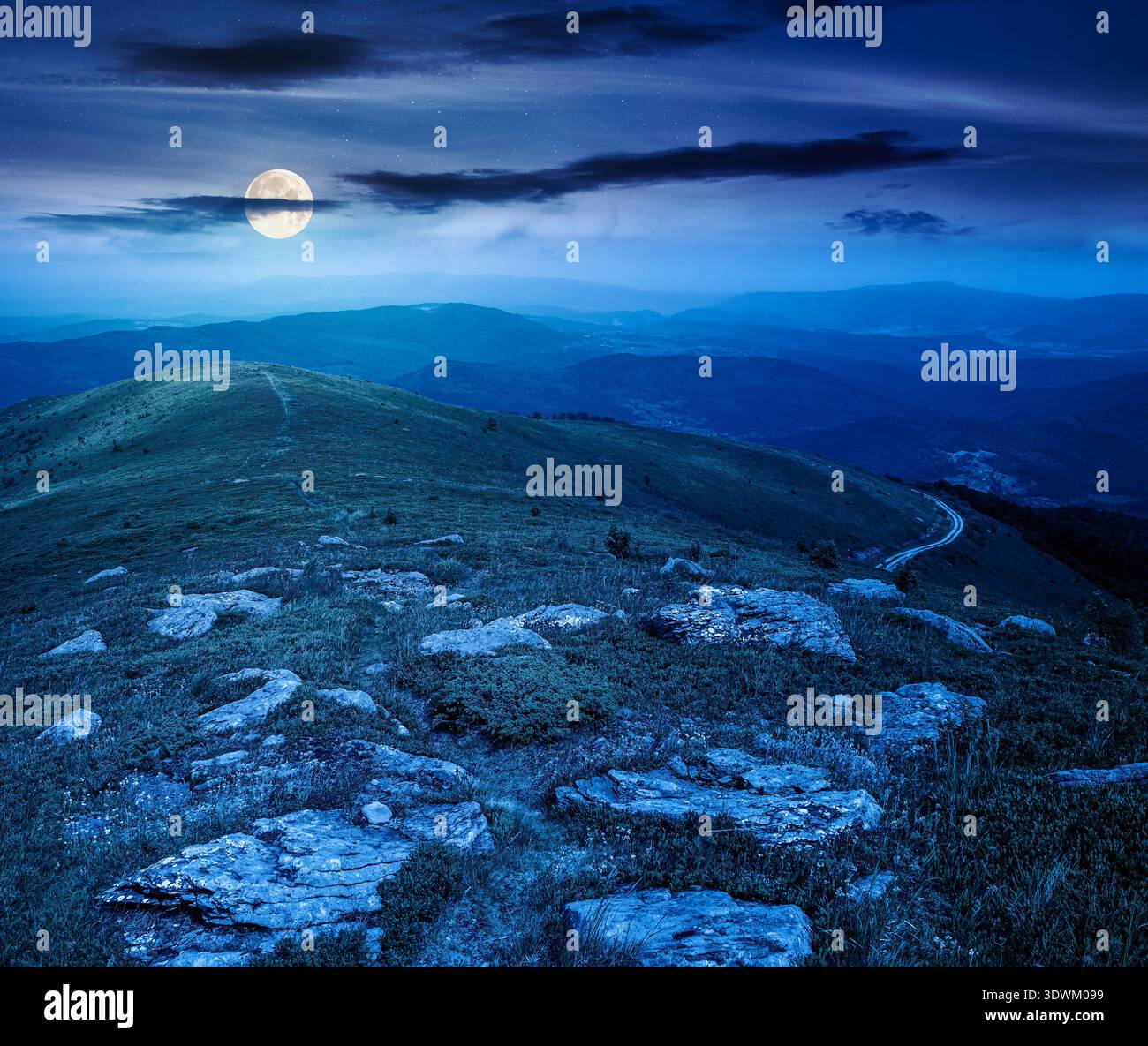 mountain landscape in summer with rocks at night. grass under dark sky in full moon light. alpine meadow and rolling hills with boulders. backdrop for Stock Photo