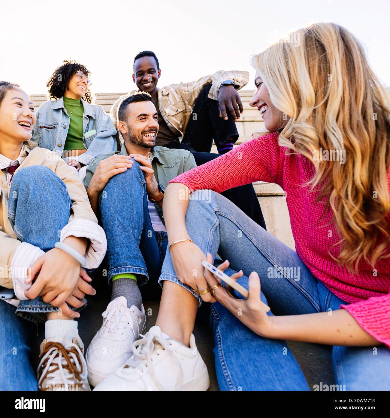 Group of young diverse student friends sitting on campus stairs talking together Stock Photo