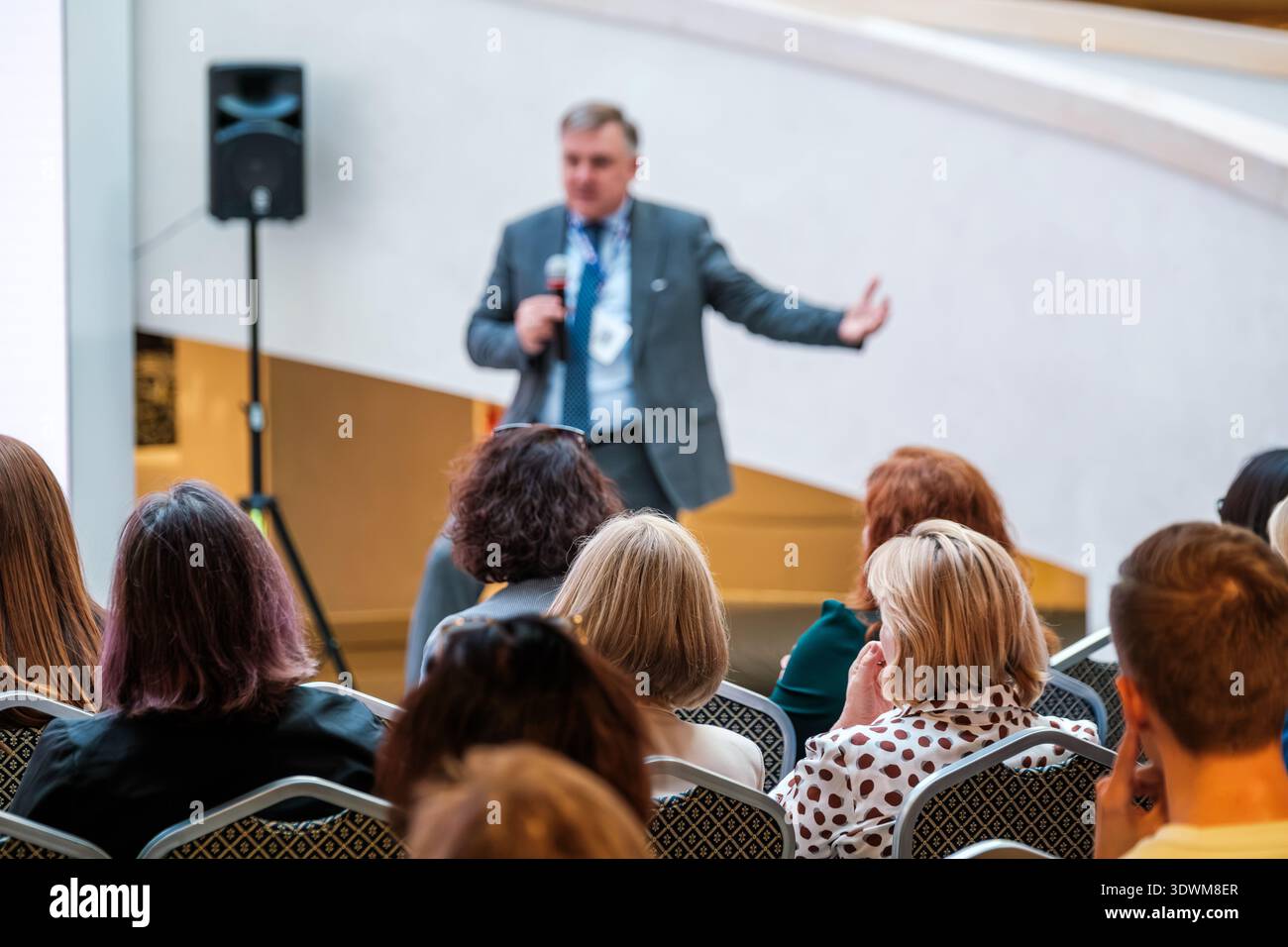 Business speaker presents to attentive audience at conference, corporate seminar atmosphere, leadership and communication focus, networking and professional development. Stock Photo