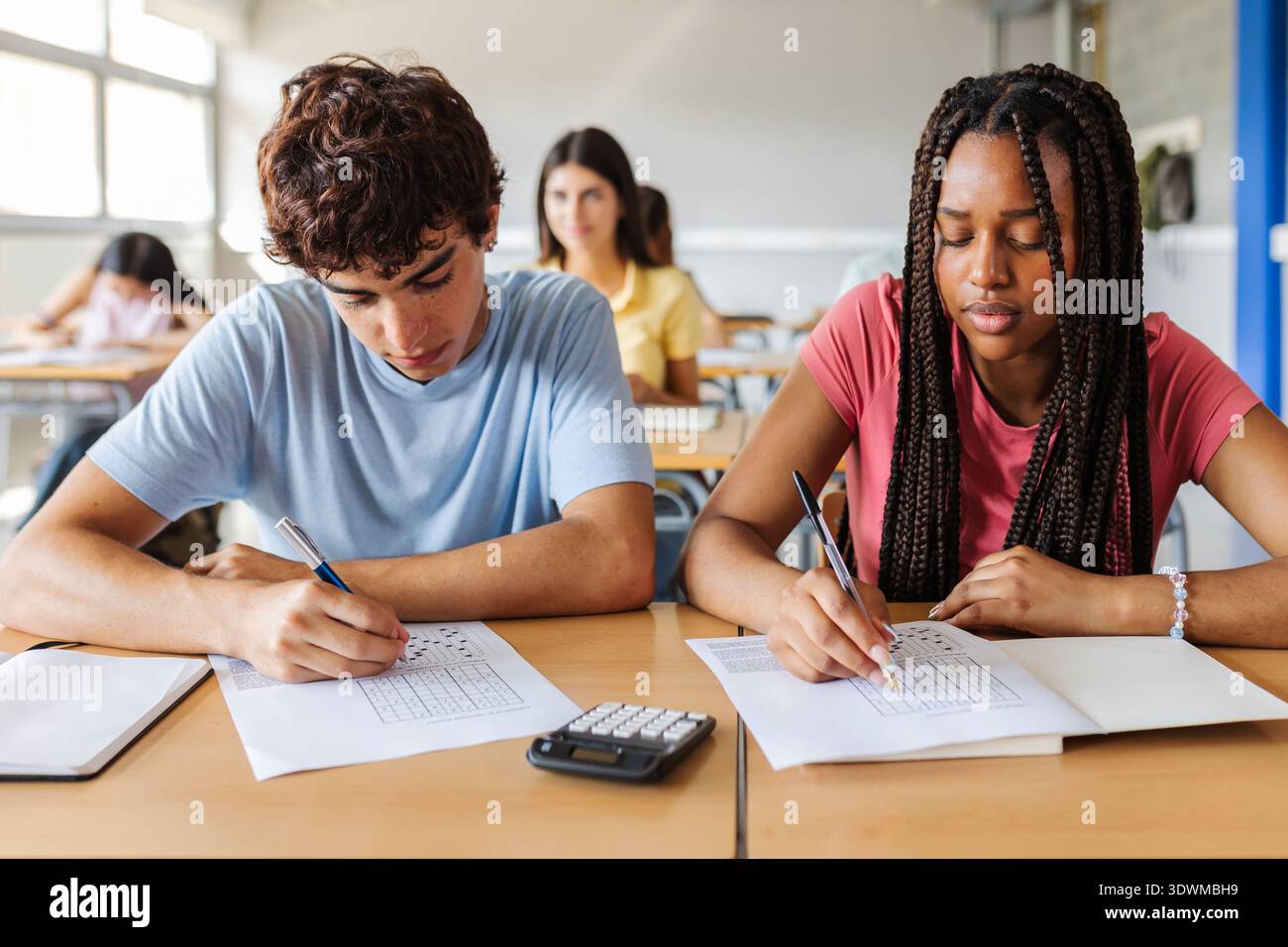 Two students writing exam together at desk Stock Photo