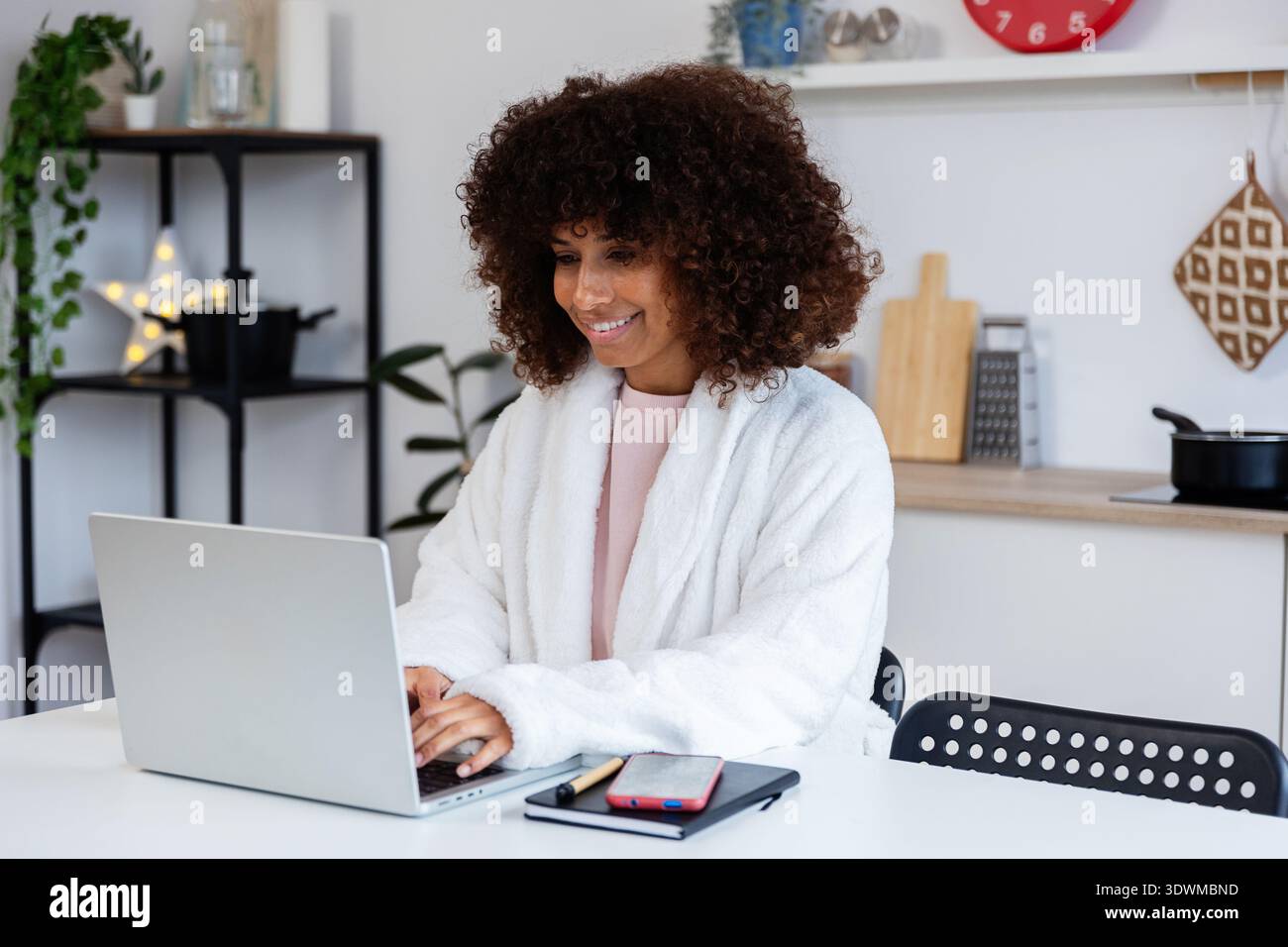 Smiling freelancer woman working from home in bathrobe using laptop Stock Photo