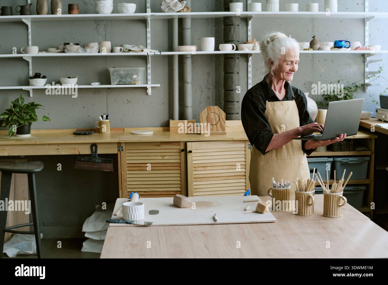 Senior Woman Using Laptop While Working in Ceramics Studio Stock Photo