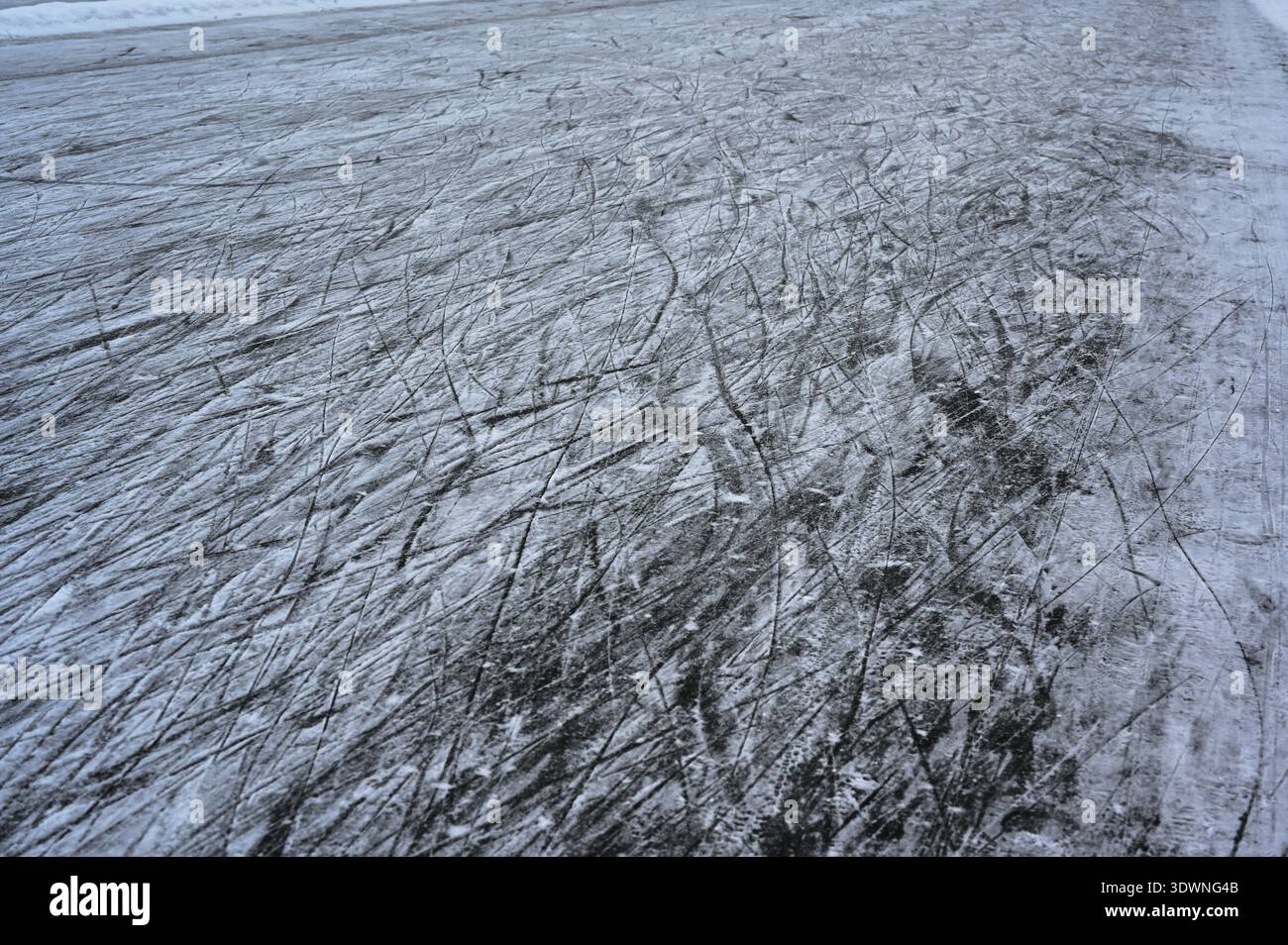 A close-up winter photograph of a frozen ice surface covered with numerous skate marks and scratches, lightly dusted with snow, creating abstract line Stock Photo