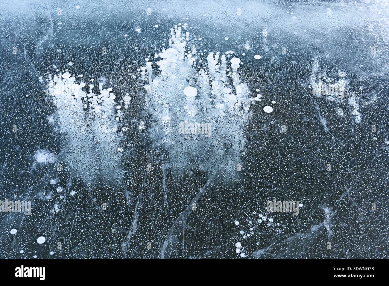 Abstract close-up photograph of frozen lake ice with trapped air bubbles and delicate cracks forming organic patterns beneath a translucent blue-gray Stock Photo