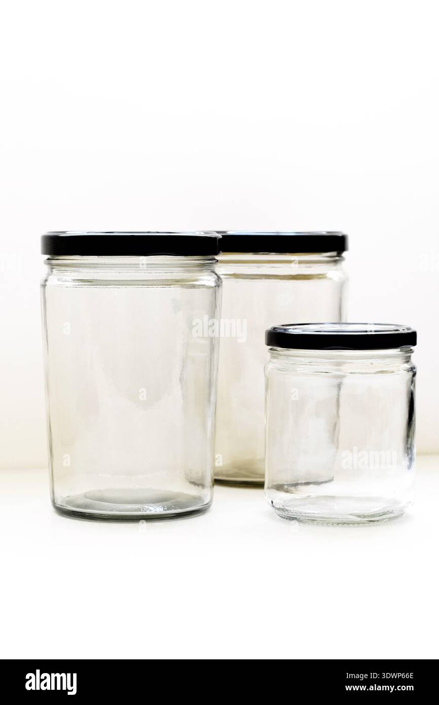 Large and small empty transparent glass bottles with black caps placed on a white table with a clean white background, ideal for cosmetic Stock Photo