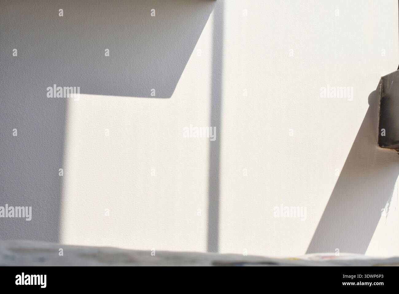 Sunlight entering through a window creating warm natural light and soft shadow patterns on a wall, minimalist interior scene with peaceful and cozy Stock Photo