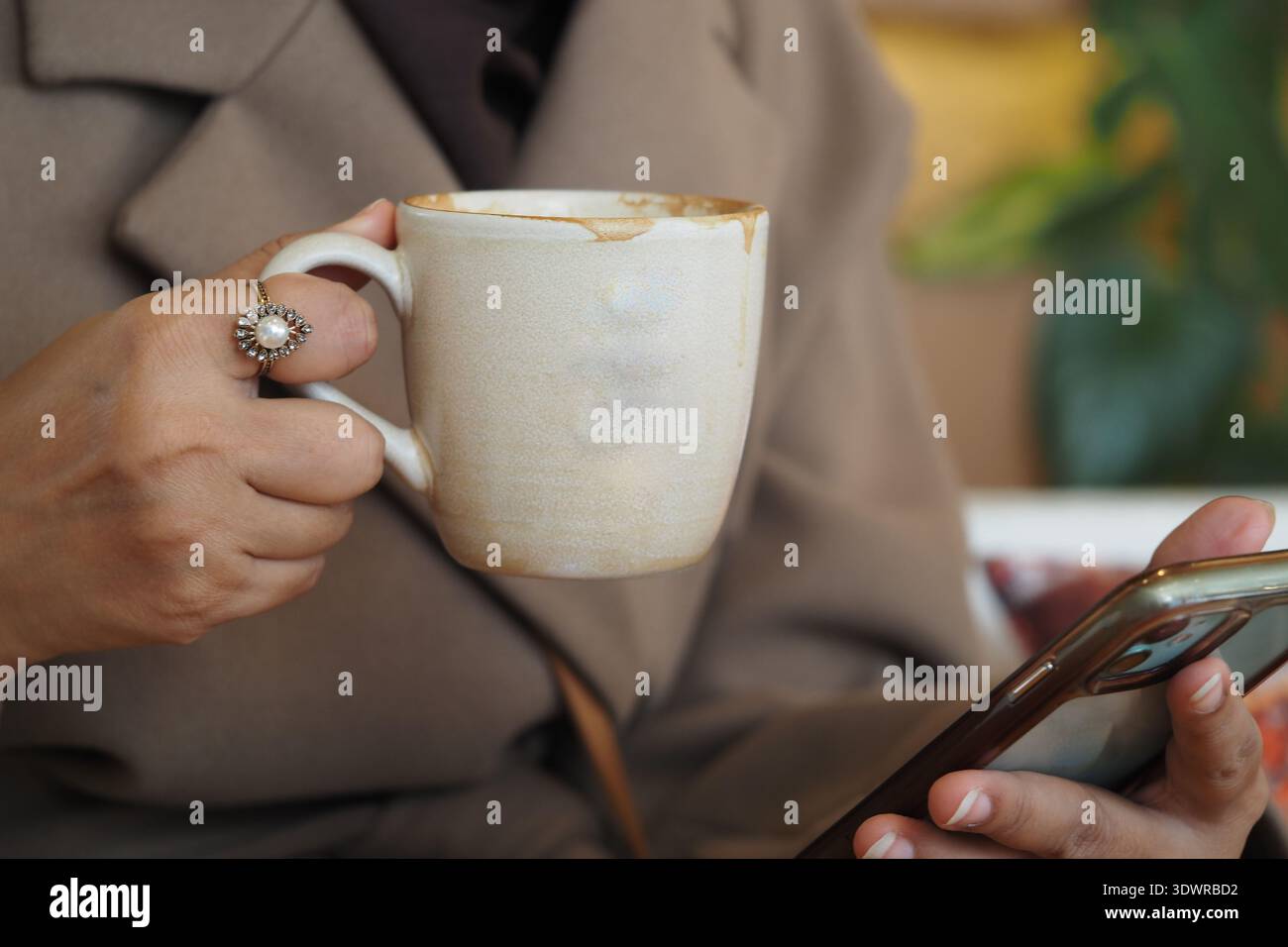 Holding a coffee cup while looking at a smartphone Stock Photo