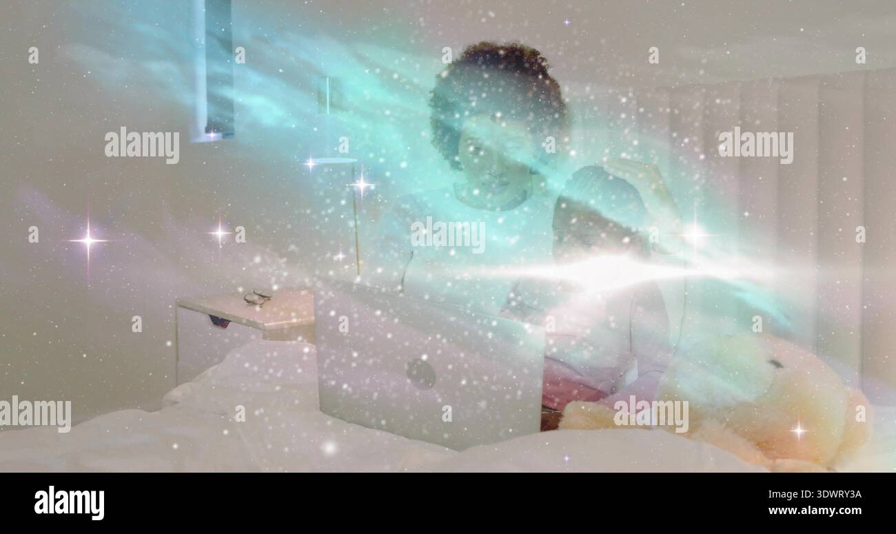 Watching woman and girl in pajamas using laptop in bedroom, with stuffed bear and aurora overlay Stock Photo