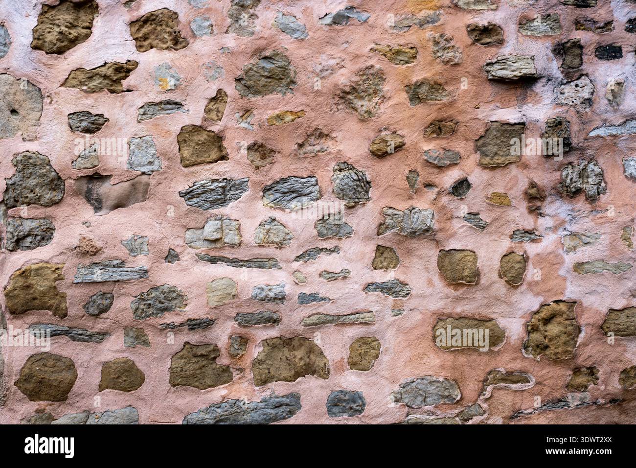 Texture of an ancient stone wall with irregular rocks embedded in weathered pink lime mortar featuring a rustic and traditional masonry style from a Stock Photo