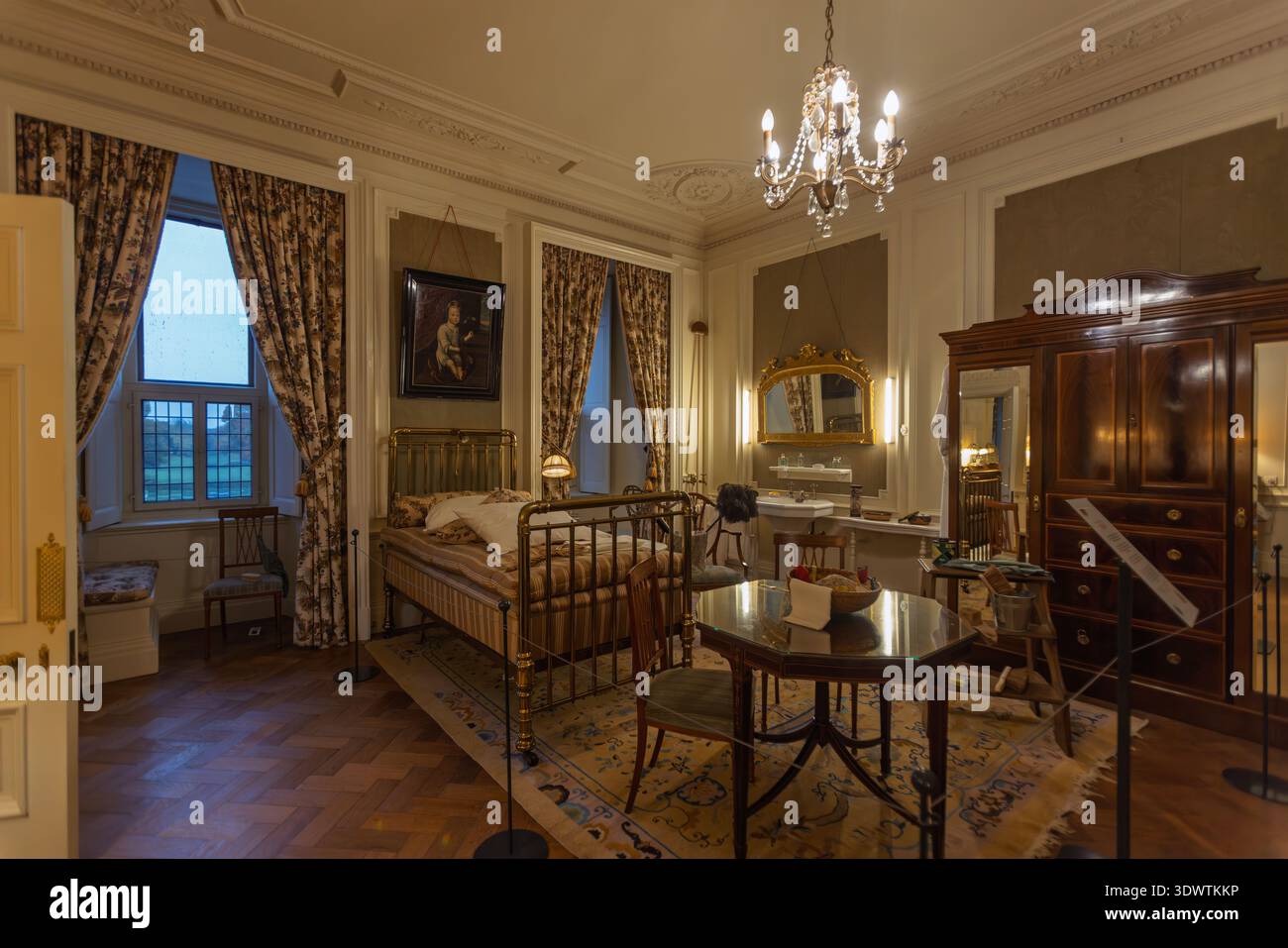 Classic castle bedroom with a brass bed, vintage vanity area, wardrobe, and large windows overlooking the estate grounds in Haarzuilens, Netherlands, Stock Photo