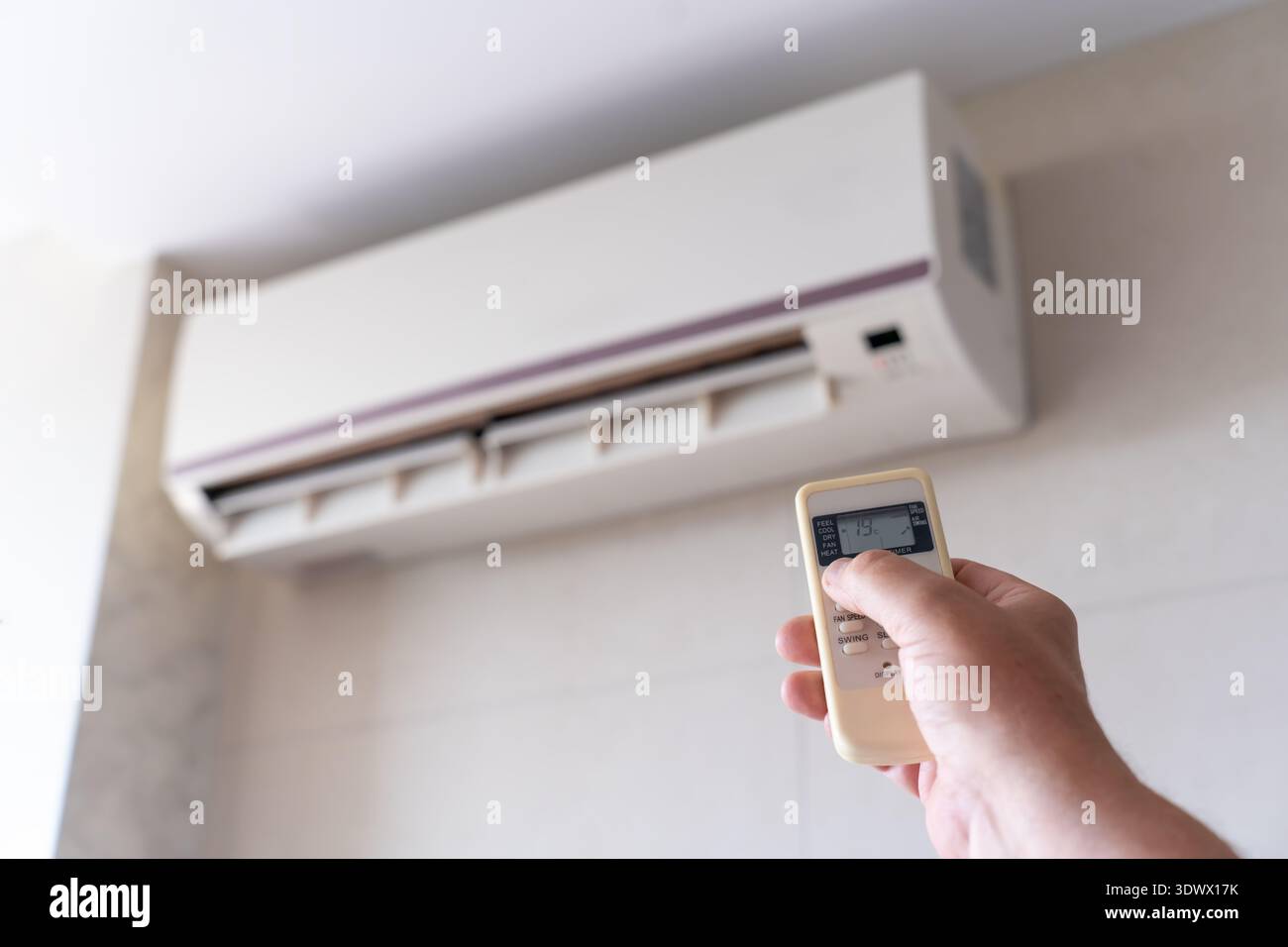 Cropped male hand operating an AC remote in a well-lit room conveys themes of smart living, seasonal regulation, and indoor calm. Scene of remote air Stock Photo