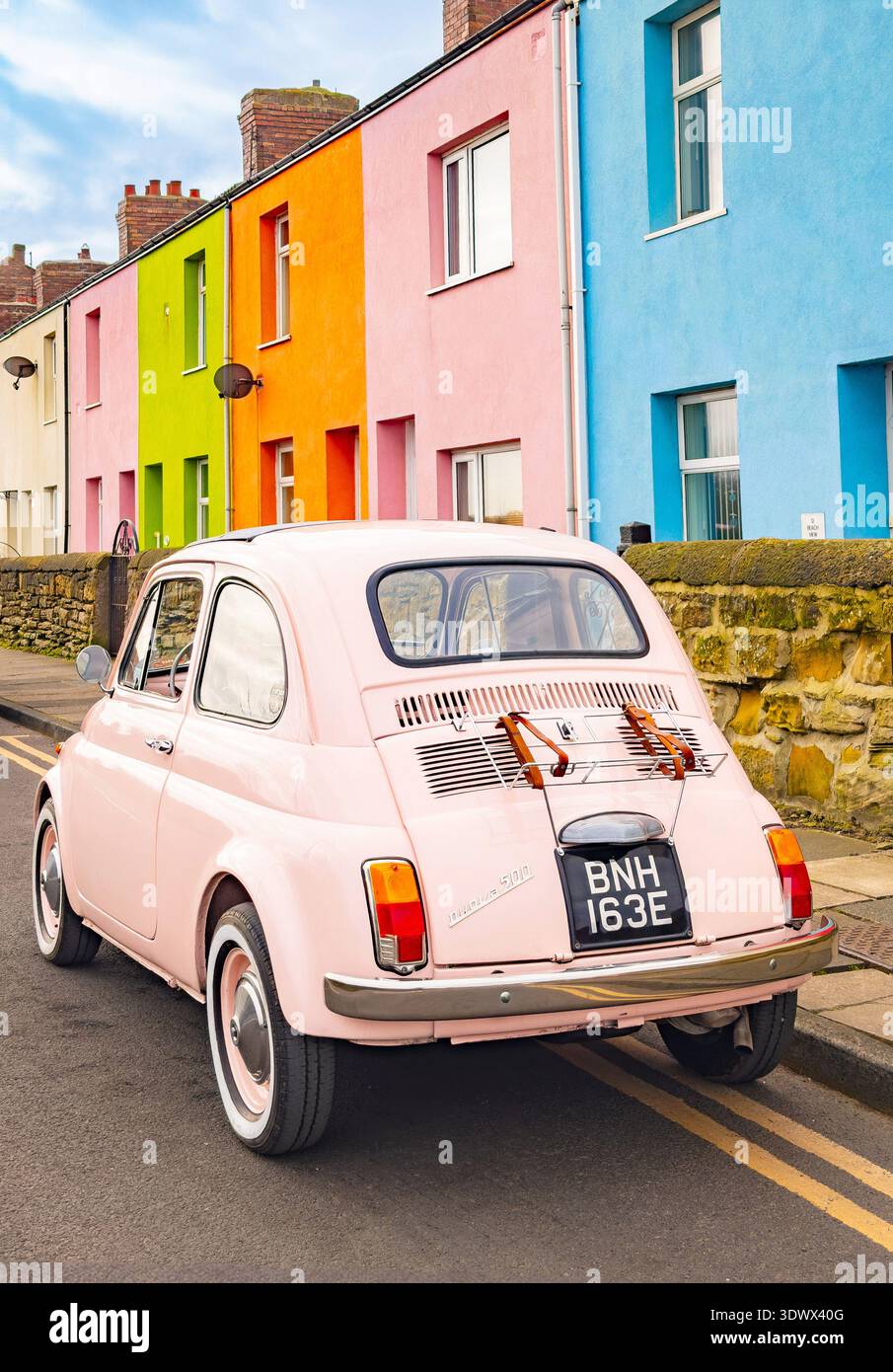 Pale pink classic  vintage Fiat 500 parked on a street against a row of brightly coloured terraced houses in Cambois northumberland - Smartphone Captured Stock Image