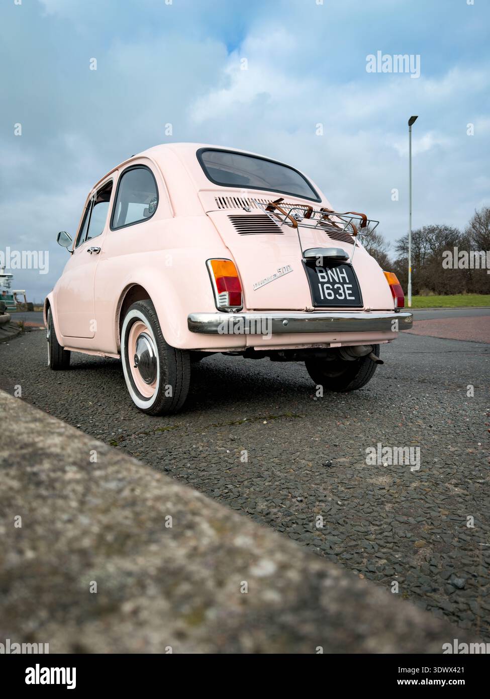 Low angle rear view of a vintage light pink Fiat 500 parked outdoors near a waterfront area Stock Photo