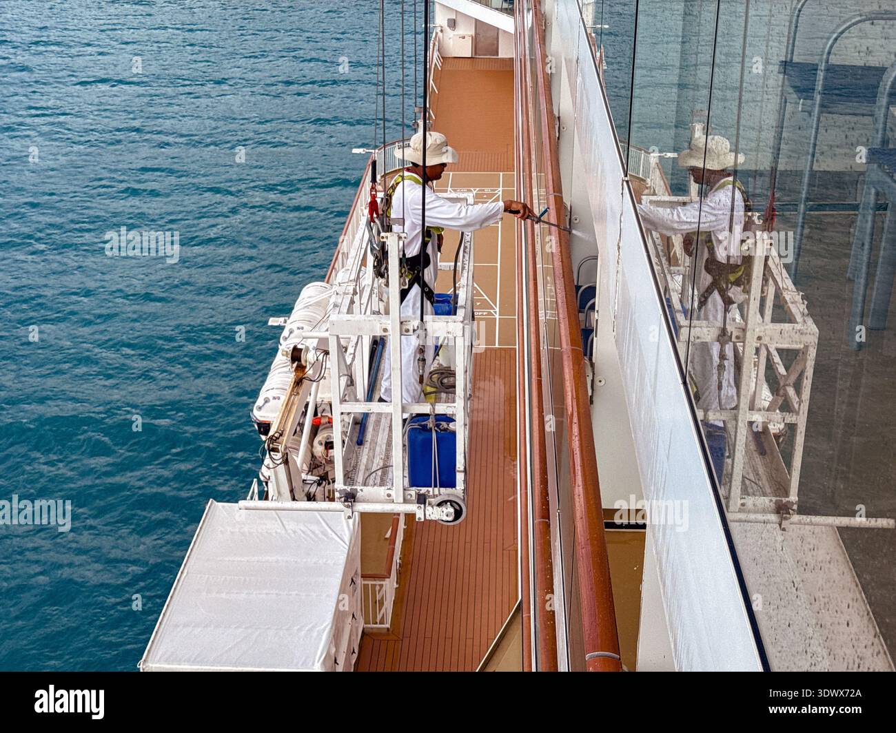 Tortola, British Virgin Islands - 18 January 2026: Member of crew of a cruise ship on a cradle platform using a pressure washer to clean windows - Smartphone Captured Stock Image