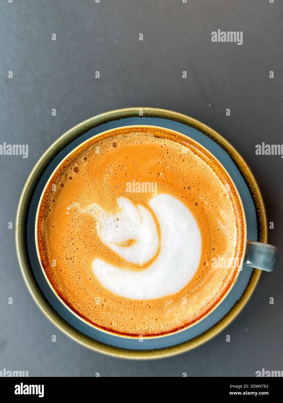 Overhead view of a cup of hot fresh frothy coffee with saucer on a table. No people. Stock Photo