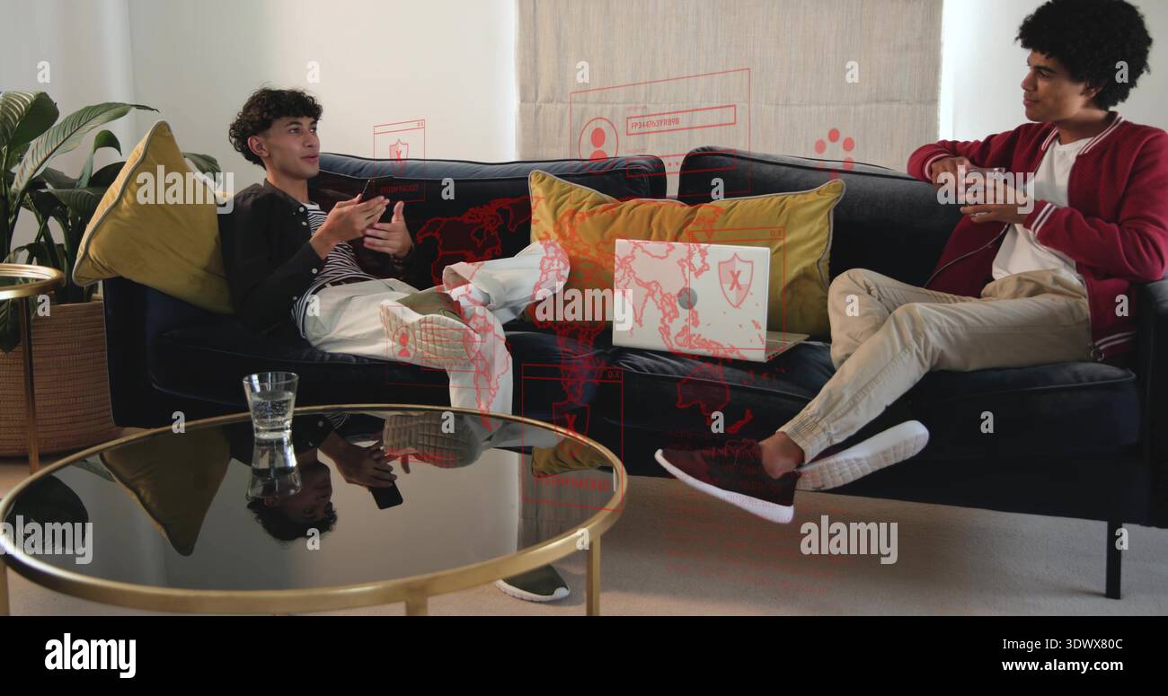 Sitting on dark blue sofa at home, two men discussing data on laptop, wearing red jacket Stock Photo