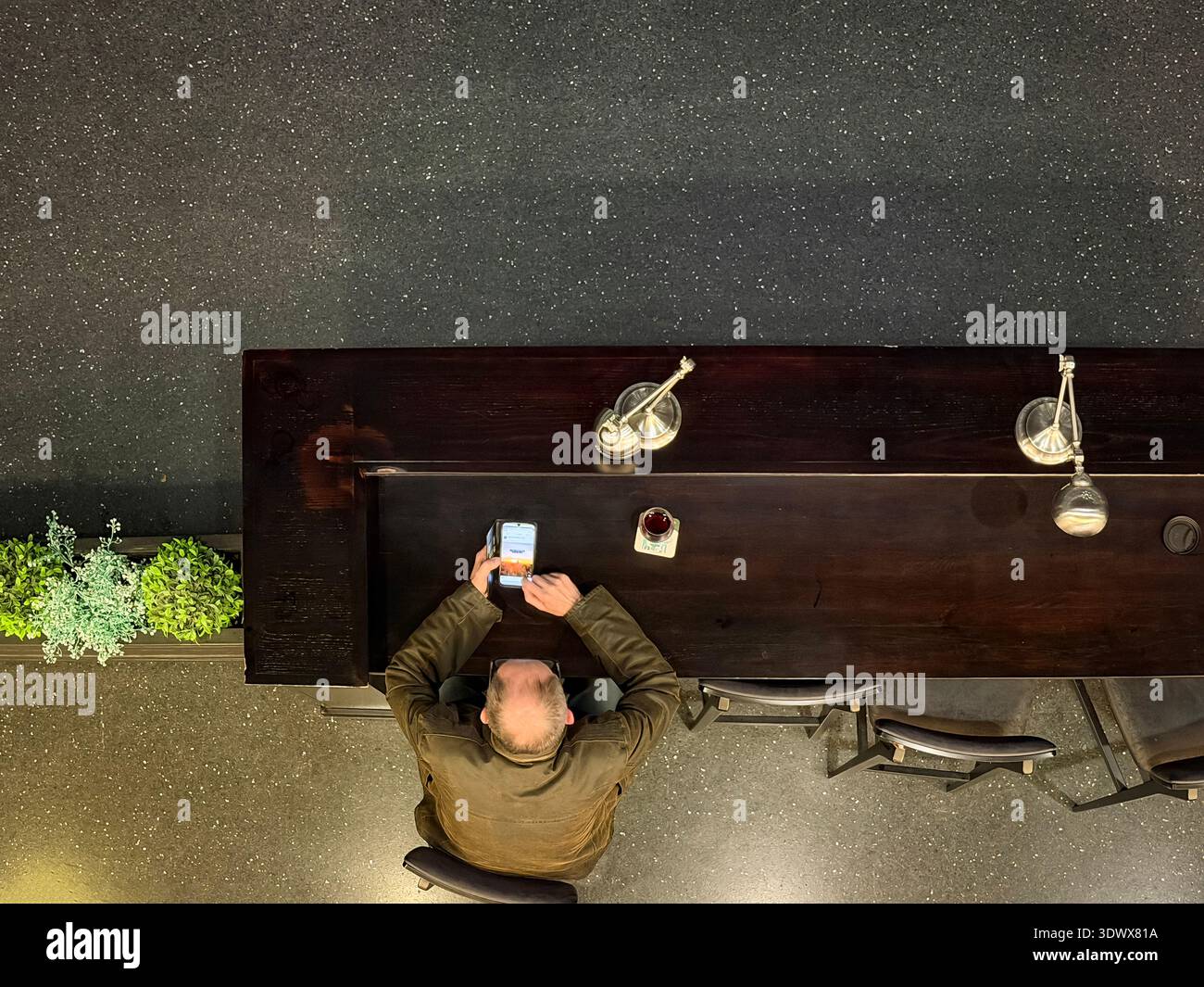 Overhead view of a man seated at a dark wooden bar or counter looking at his smartphone glasshouse concert venue uk - Smartphone Captured Stock Image
