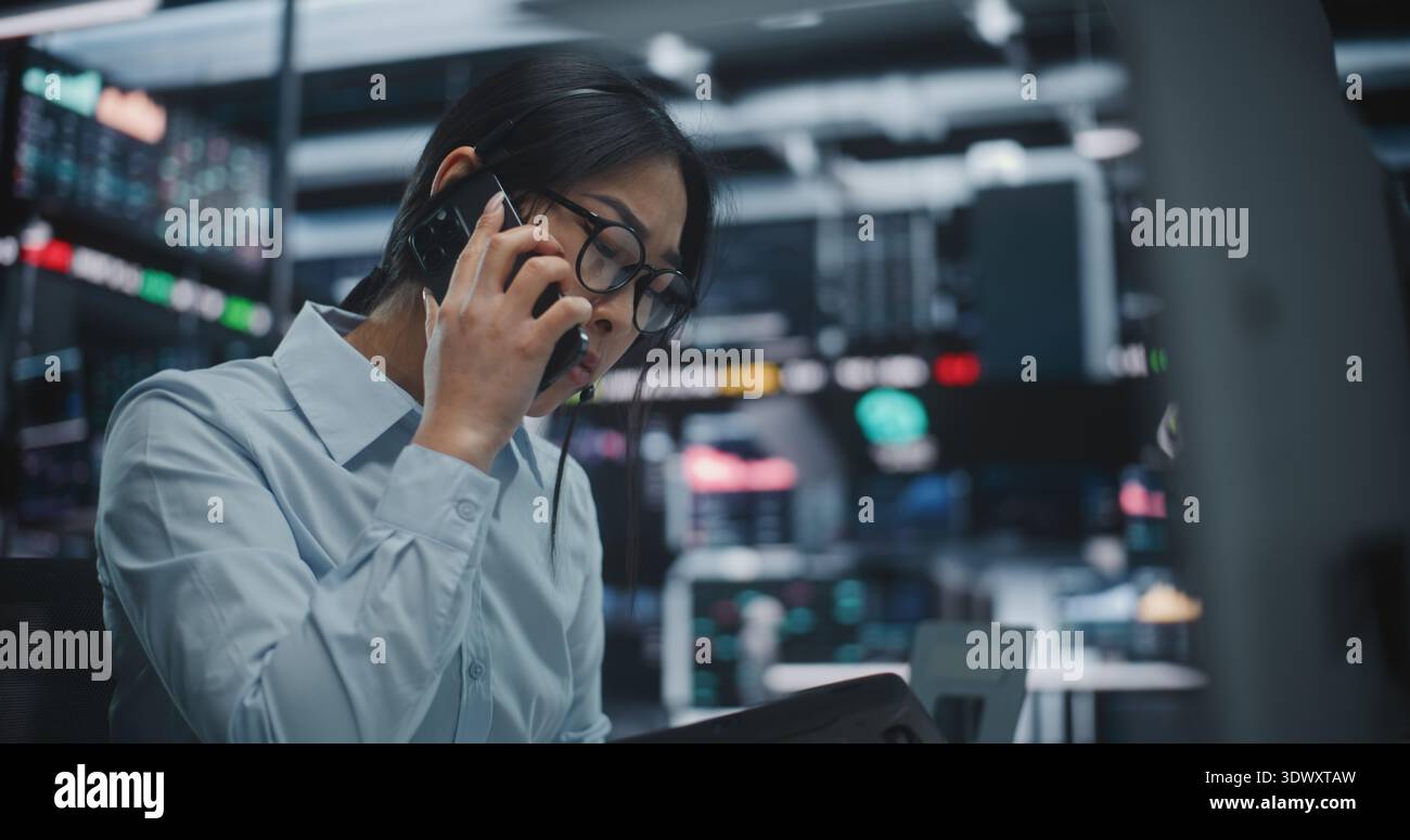 Asian Woman Frantically Cross References Real Time Financial Data on Multi Monitor Workstation and Tablet. Female Reports Critical Market Information Contact on Smartphone. Urgent Communication. Stock Photo
