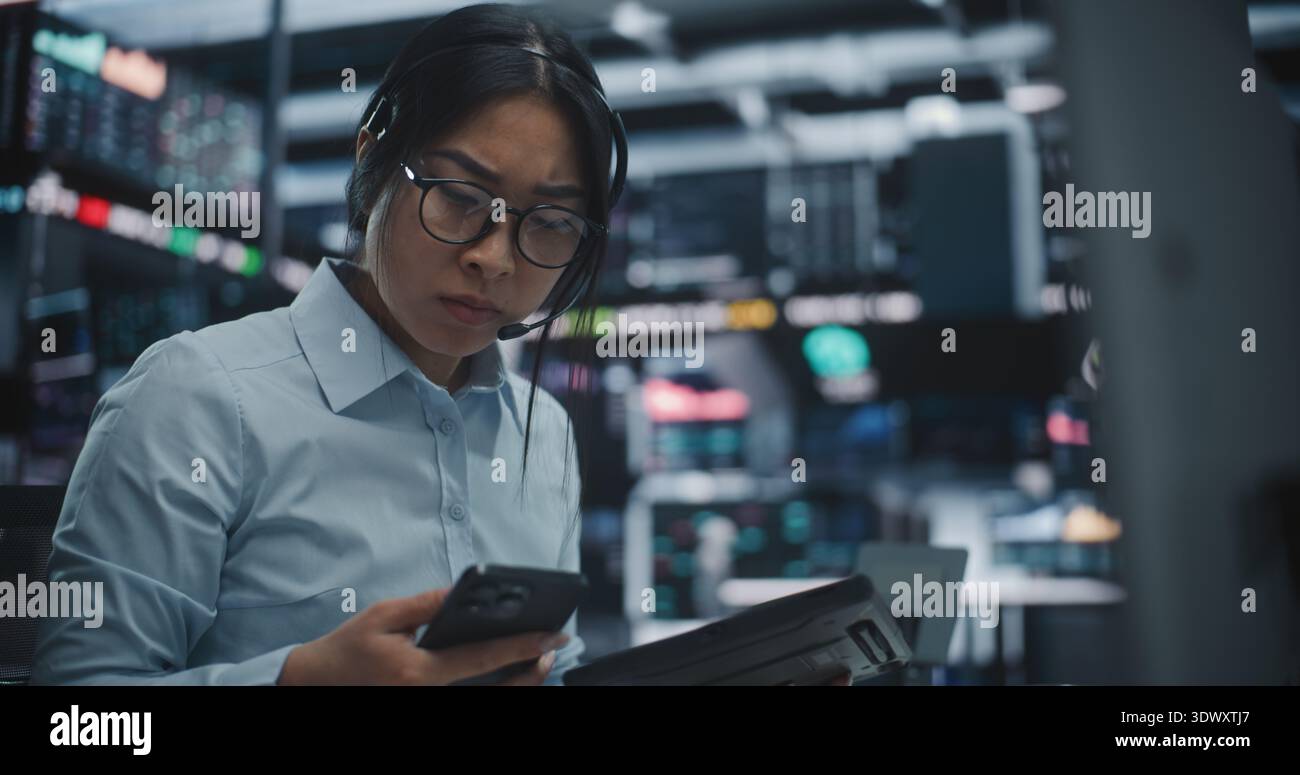 Asian Woman Frantically Cross References Real Time Financial Data on Multi Monitor Workstation and Tablet. Female Reports Critical Market Information Contact on Smartphone. Urgent Communication. Stock Photo