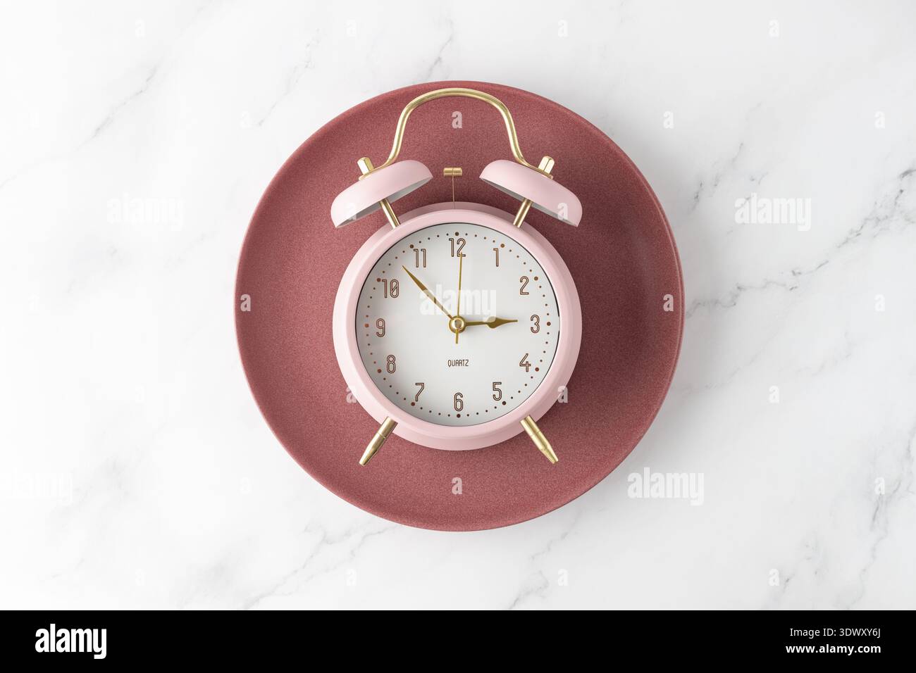 Pink alarm clock on retro red plate on white marble table background. Time to food. Meal on time as element of healthy diet. Stock Photo