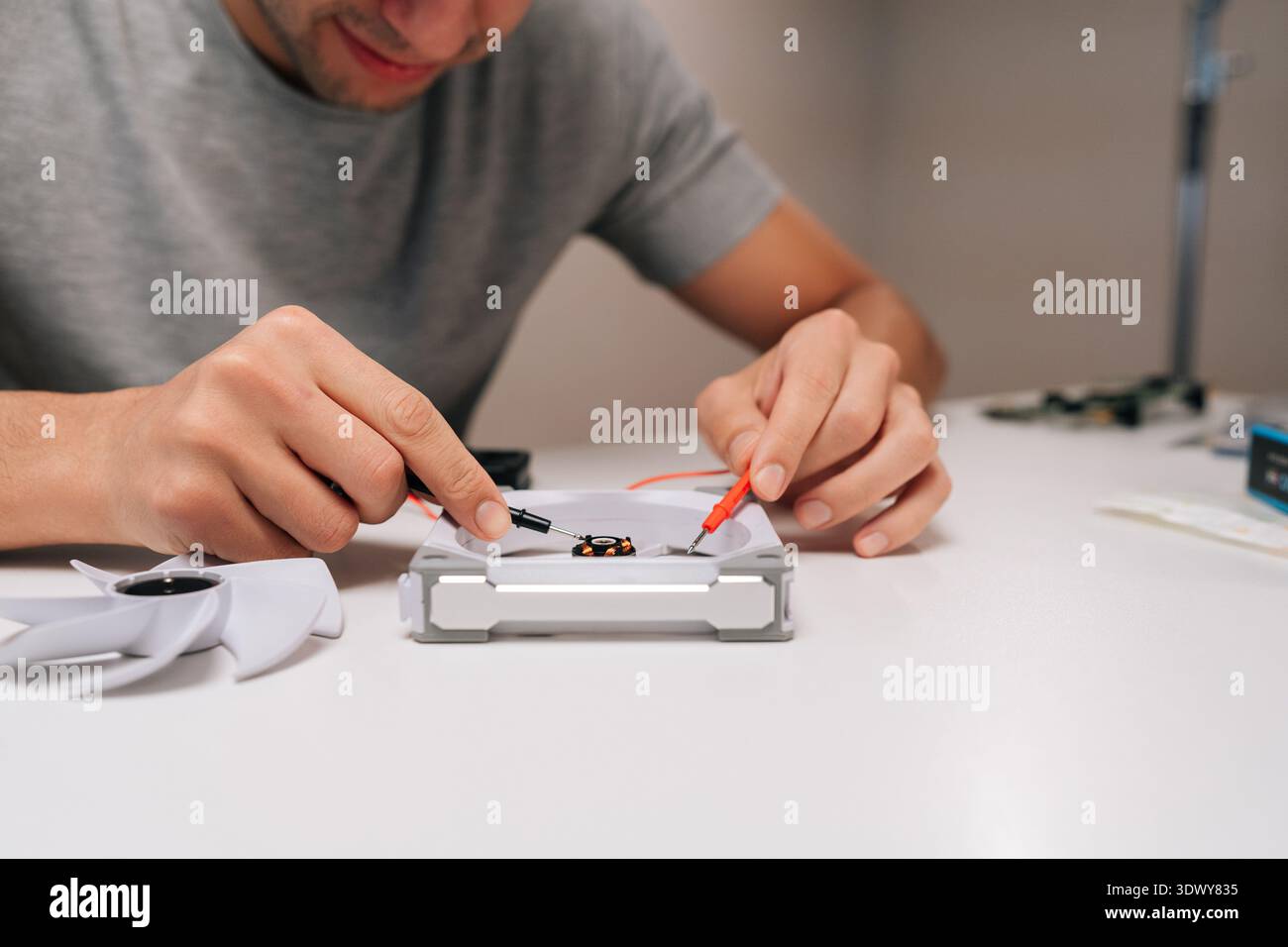 Technician working on computer cooling fan, testing motor with multimeter, checking electronic components during hardware repair and maintenance Stock Photo