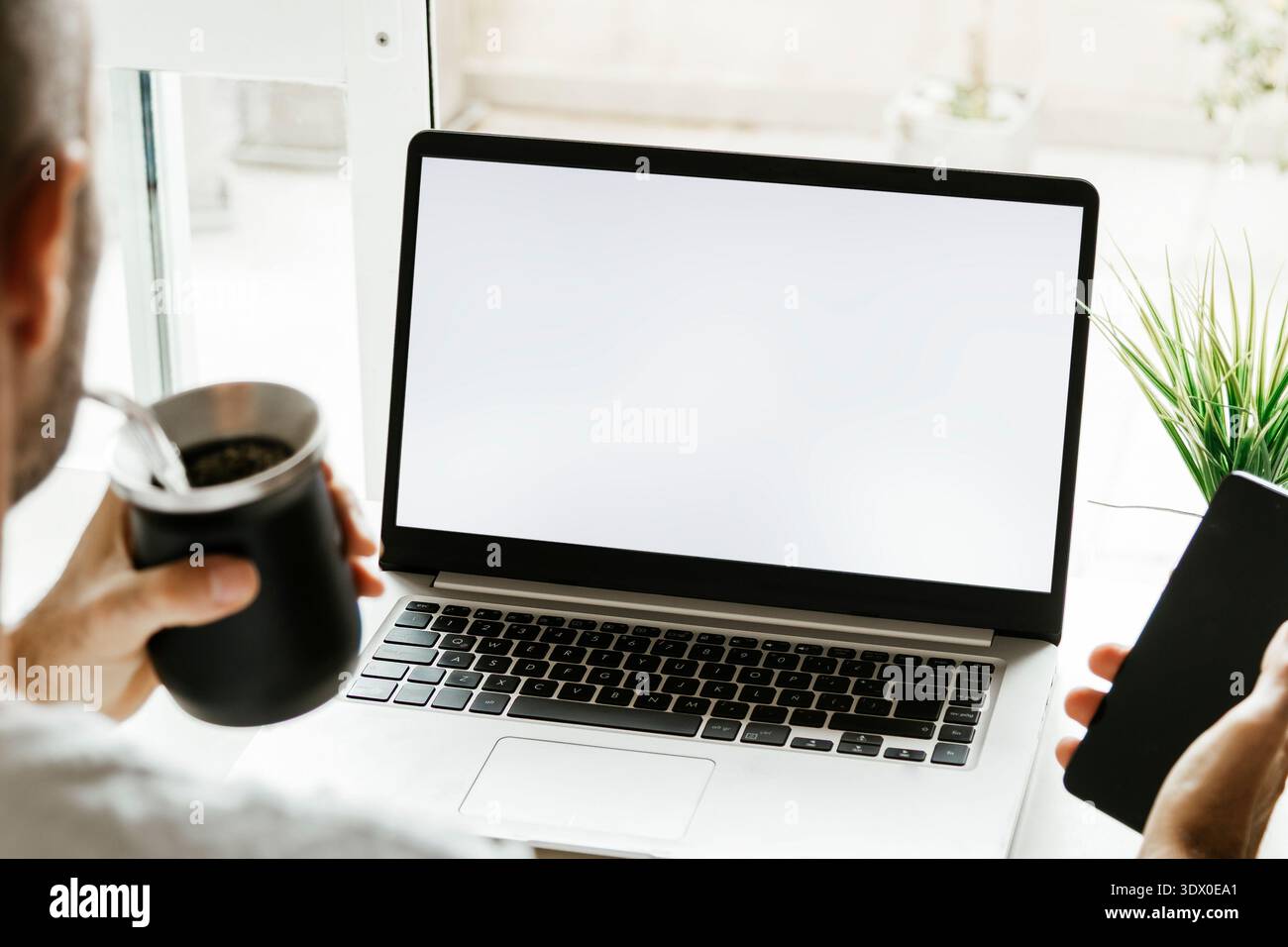 Man hands using laptop with empty screen. Blank white screen. Argentinian user using a computer while drinking yerba mate. Photo ready for mockup. Stock Photo
