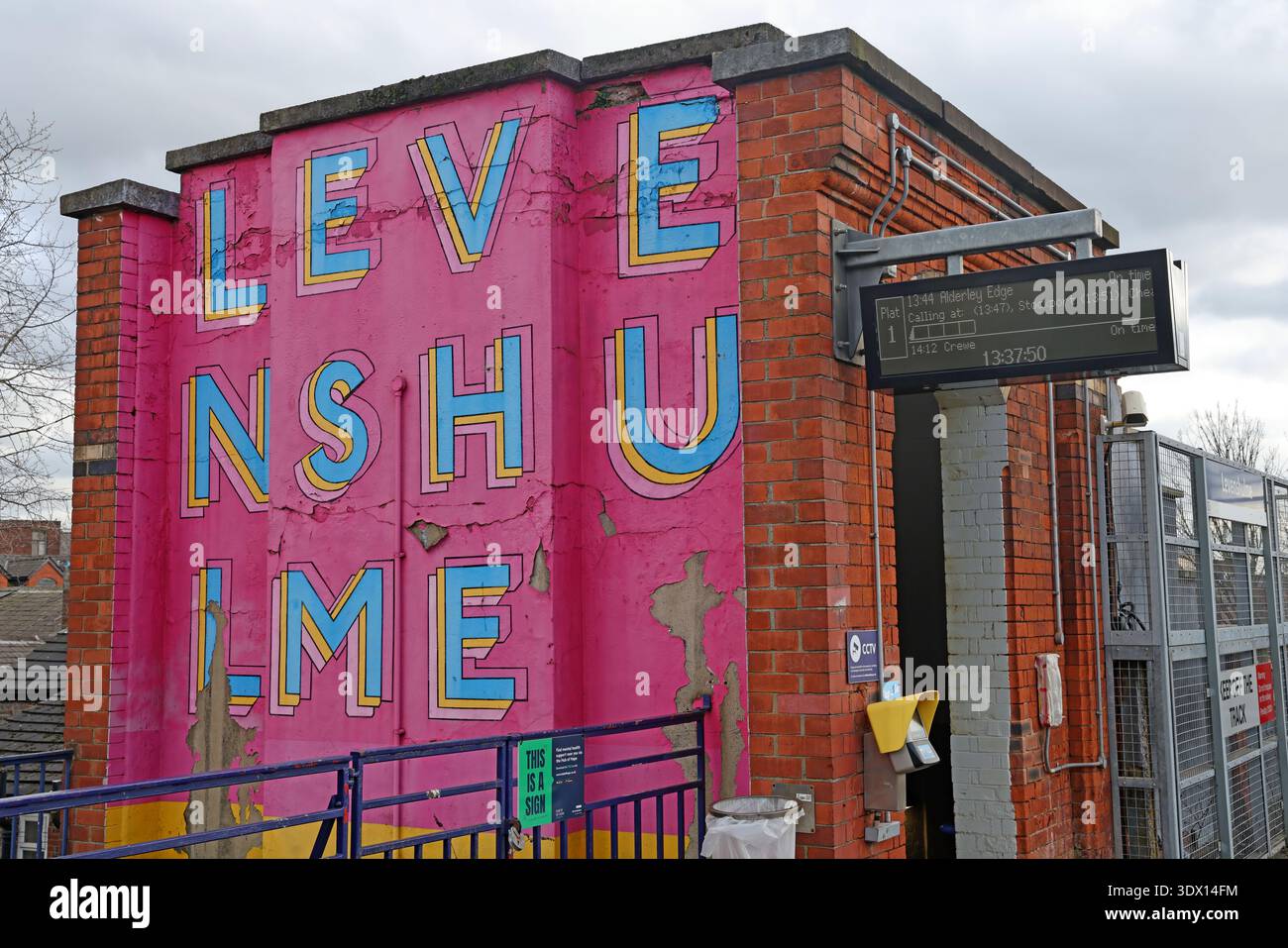 Colourful entrance to Levenshulme railway station on Albert Road, Manchester, with large pink painted wall lettering and platform access. Stock Photo