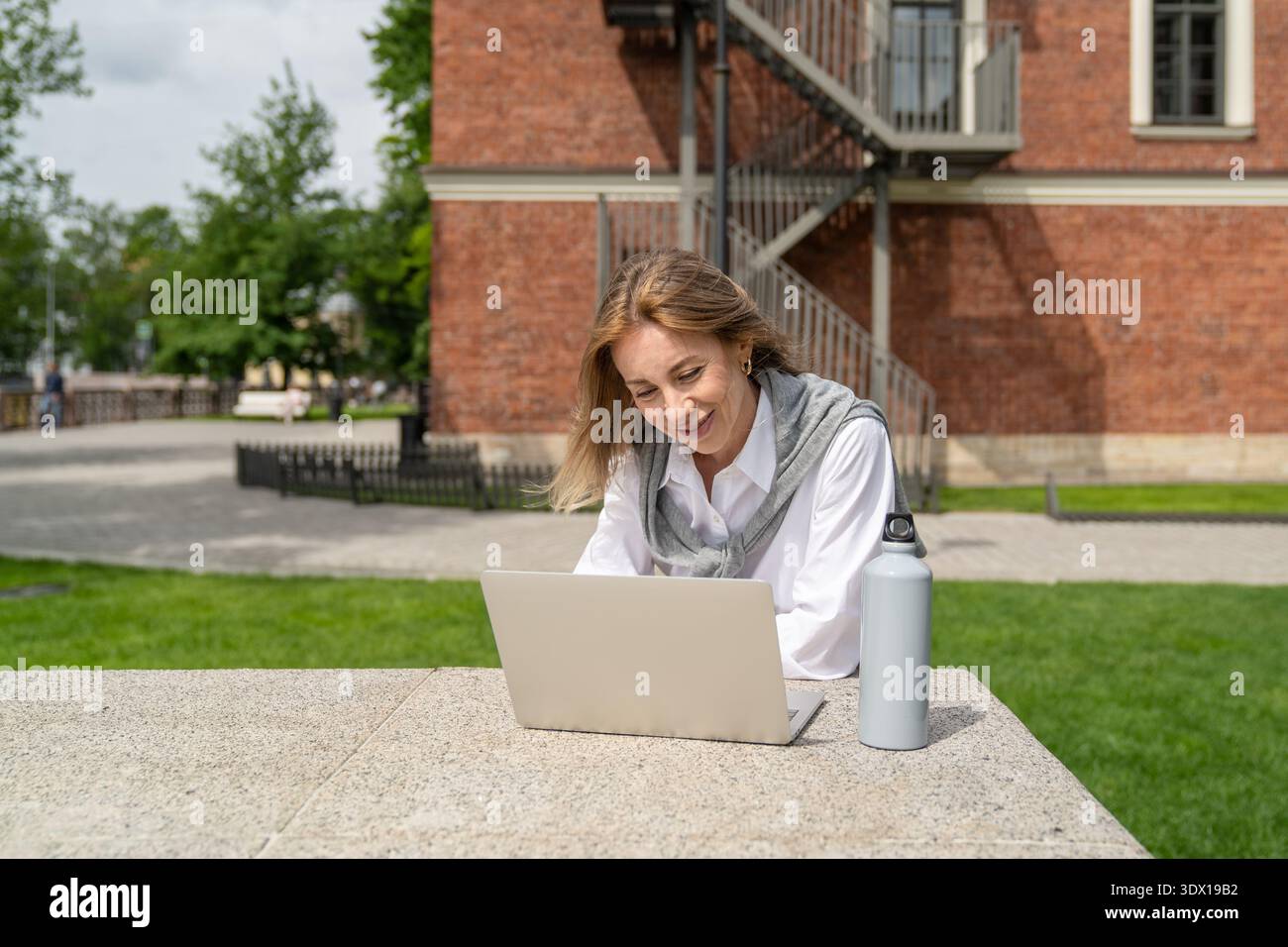 Positive businesswoman working on remote using laptop outdoors in park, talking by video call online Stock Photo
